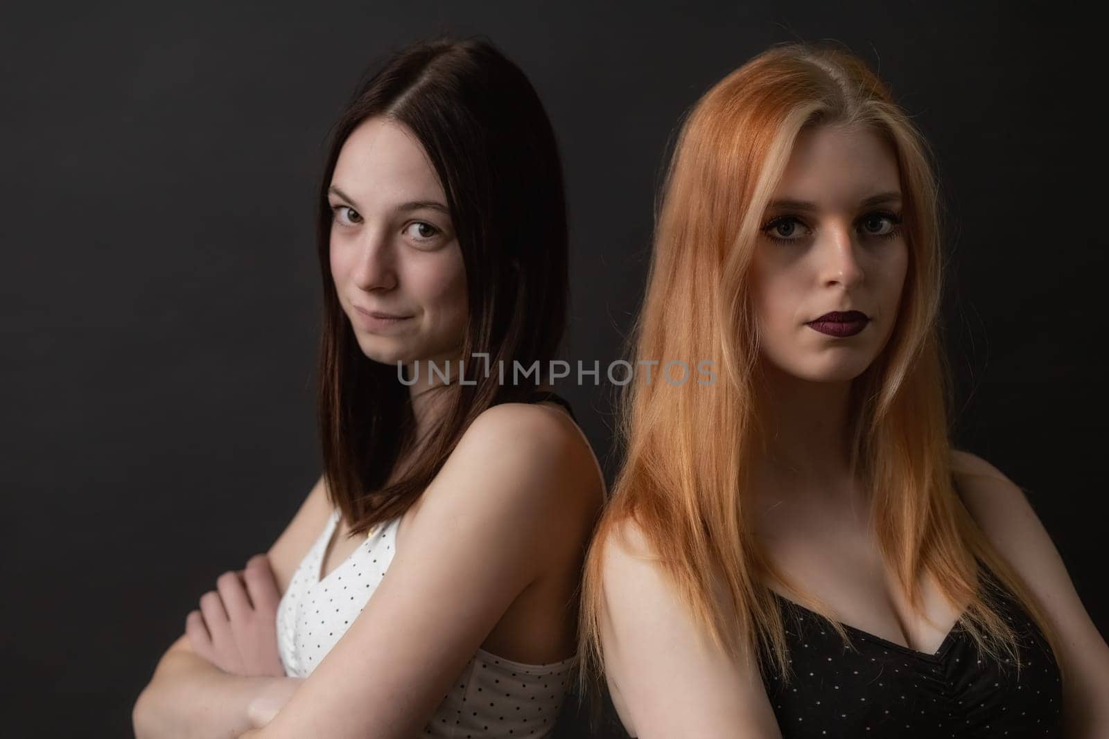 Couple of young women is posing on the black background. Horizontally.