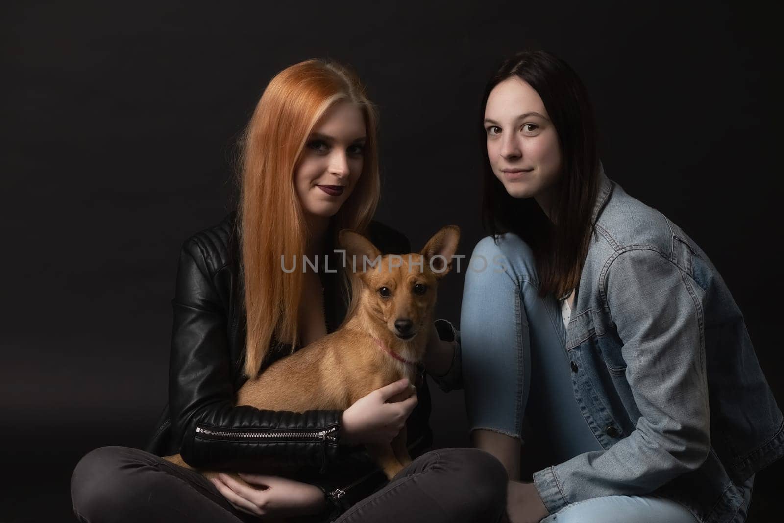 Pair of young smiling women holding brown dog. All are looking at the camera.