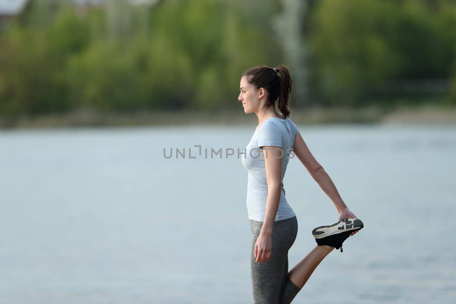 Side view portrait of a sportswoman stretching leg after sport in a lake