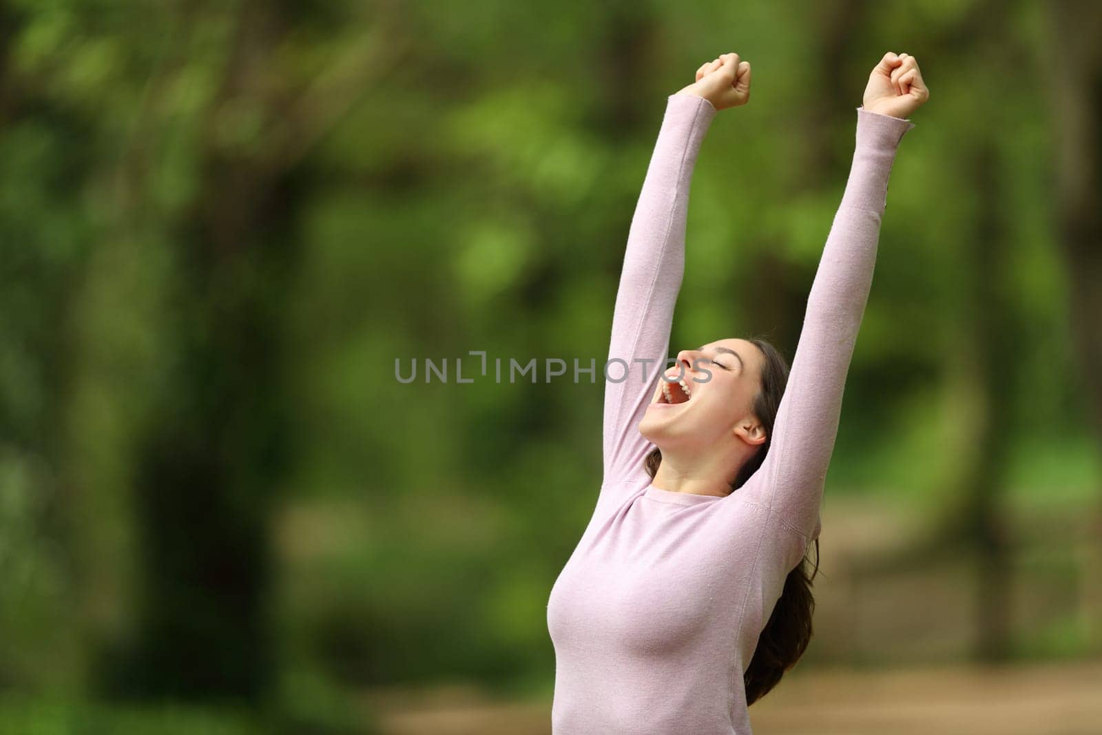 Excited woman raising arms and screaming celebrating in a green forest