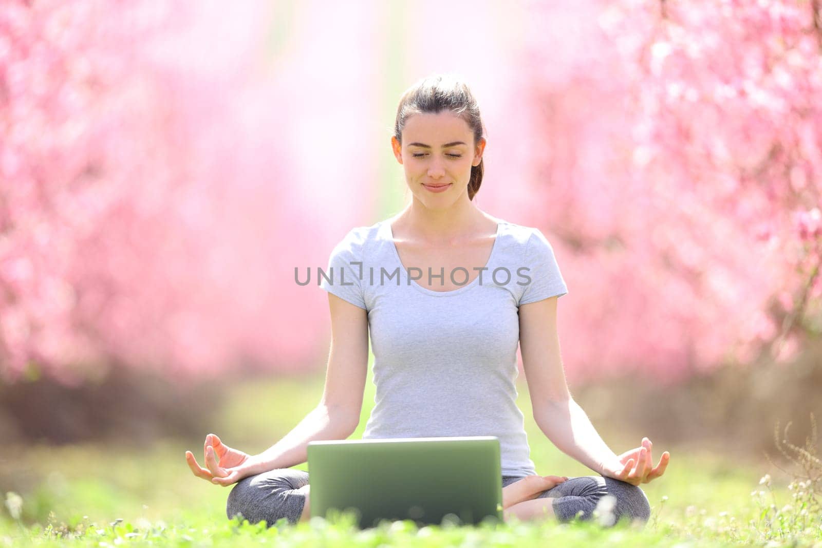 Front view portrait of a happy yogi e-learning yoga with a laptop in a field in springtime