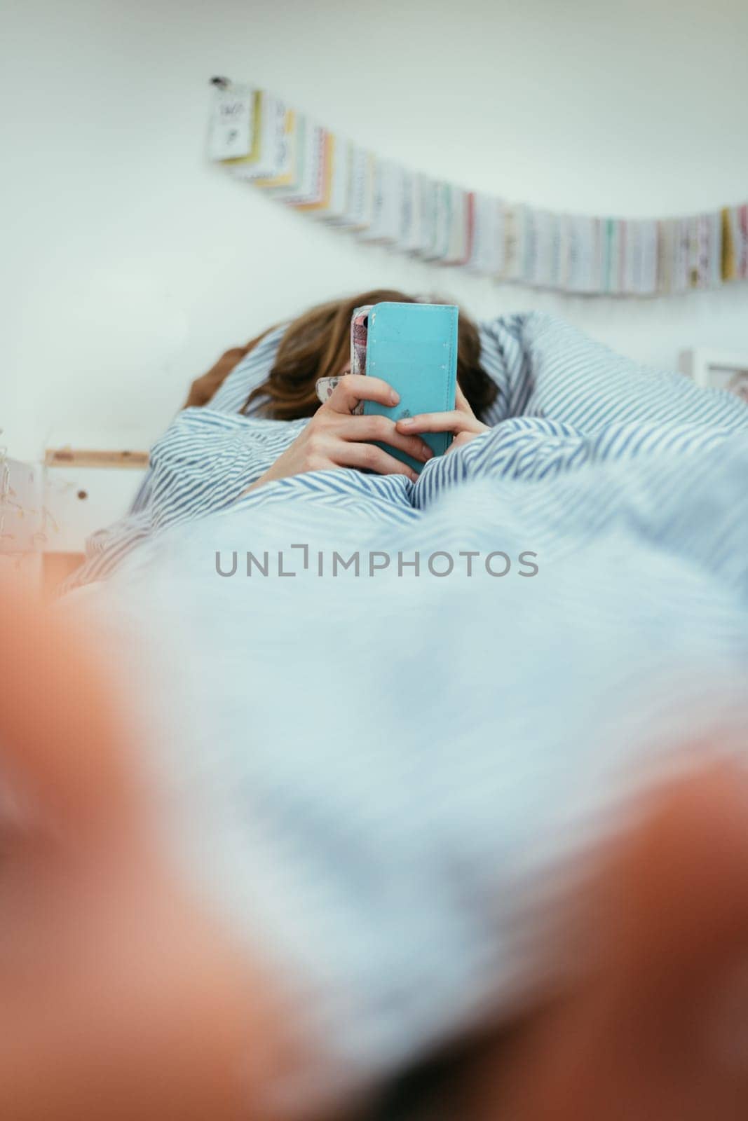 Girl lying in bed is using her smartphone, smartphone in the foreground, blurry background
