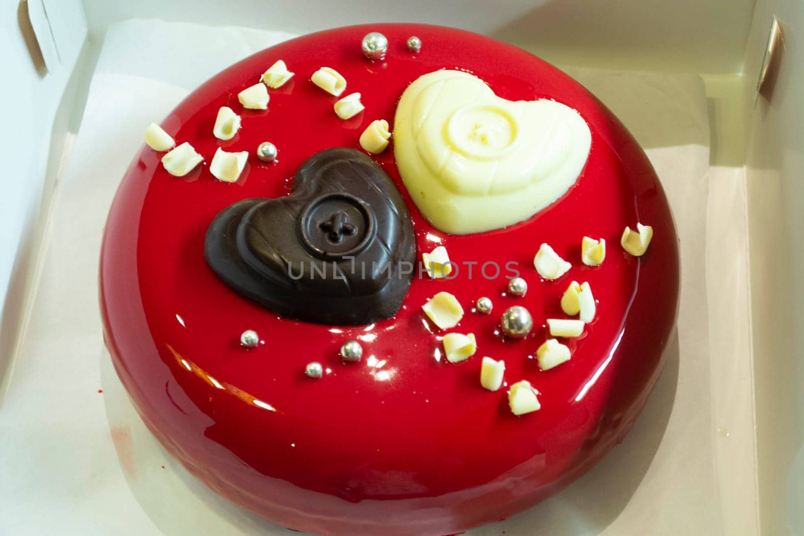 Trendy mousse cake with red mirror glaze decorated with light and dark hearts.