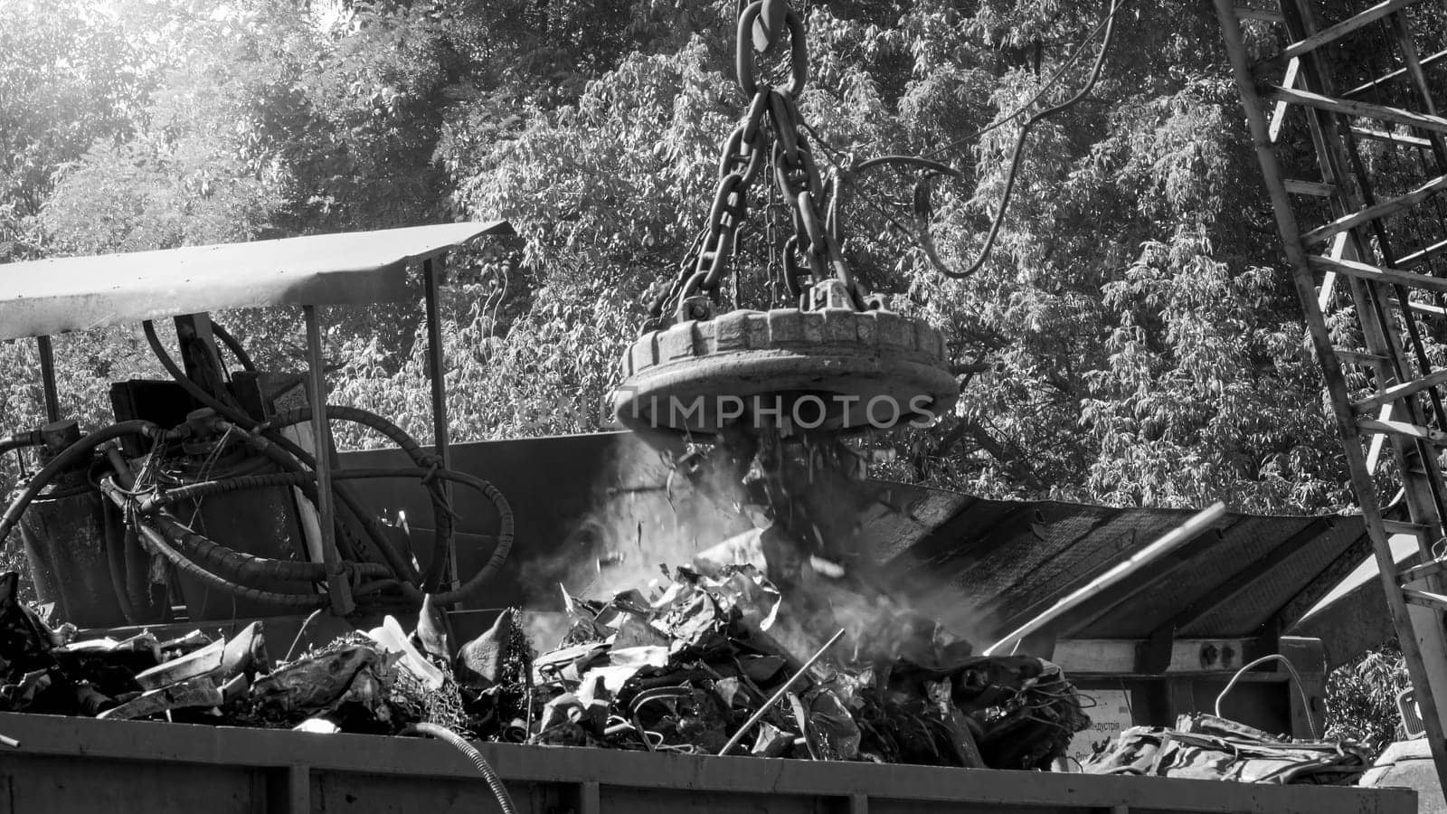 Black and white photo of big industrial electric magnet sorting metal scrap on the junkyard