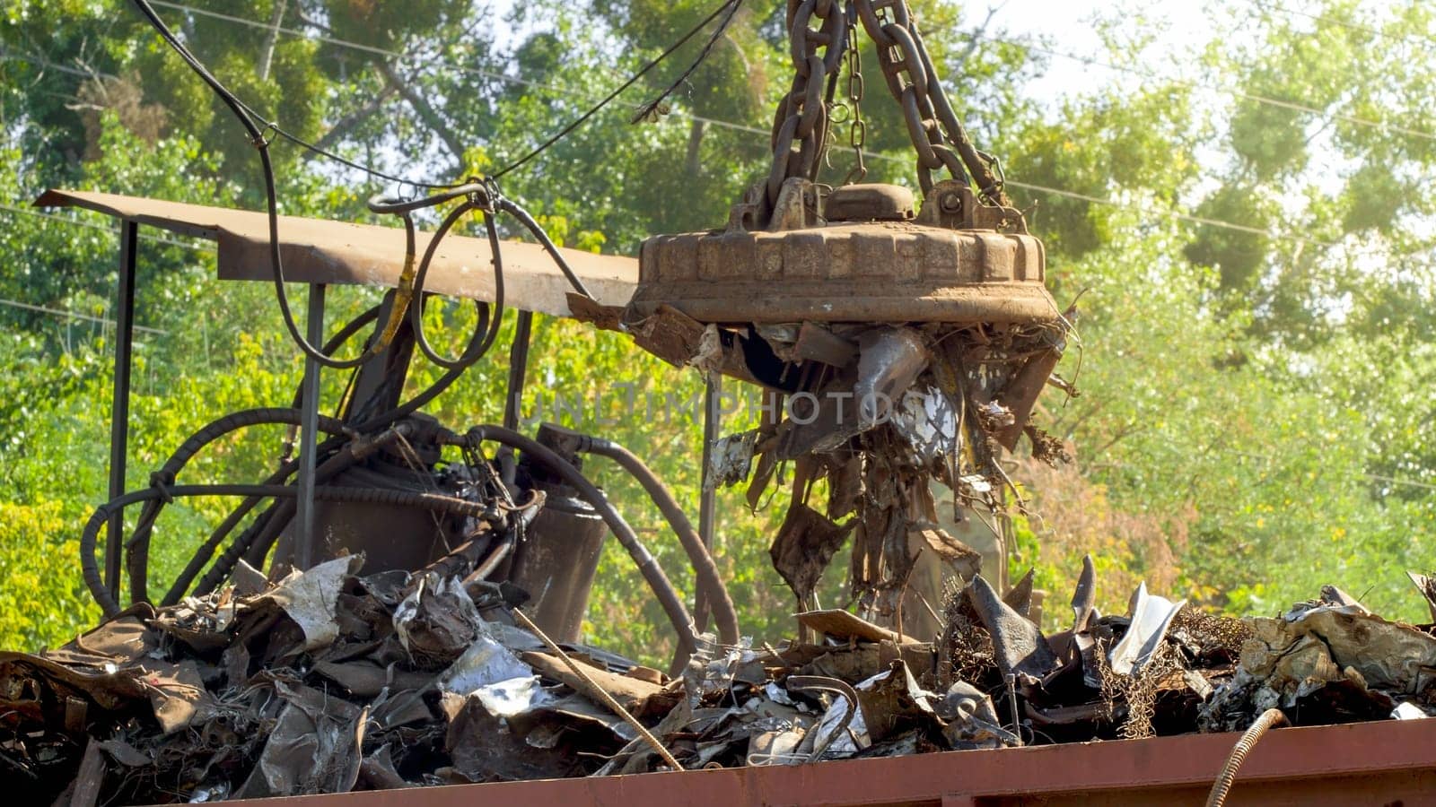 Image of big electric magnet sorting and lifting metal part and waste on the outdoor dump