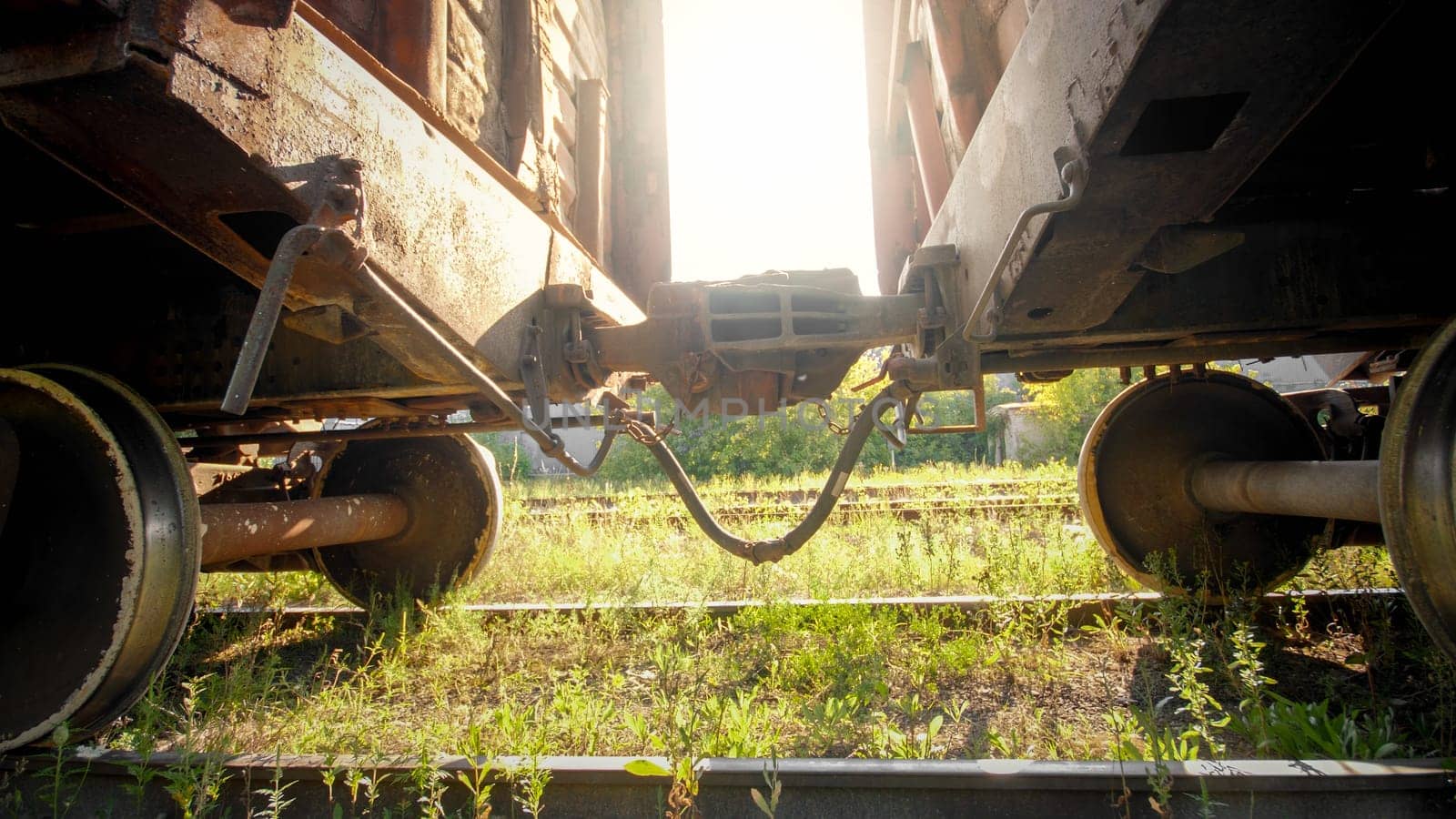 Metal coupler connecting two heavy cargo train wagons on railroad at sunset