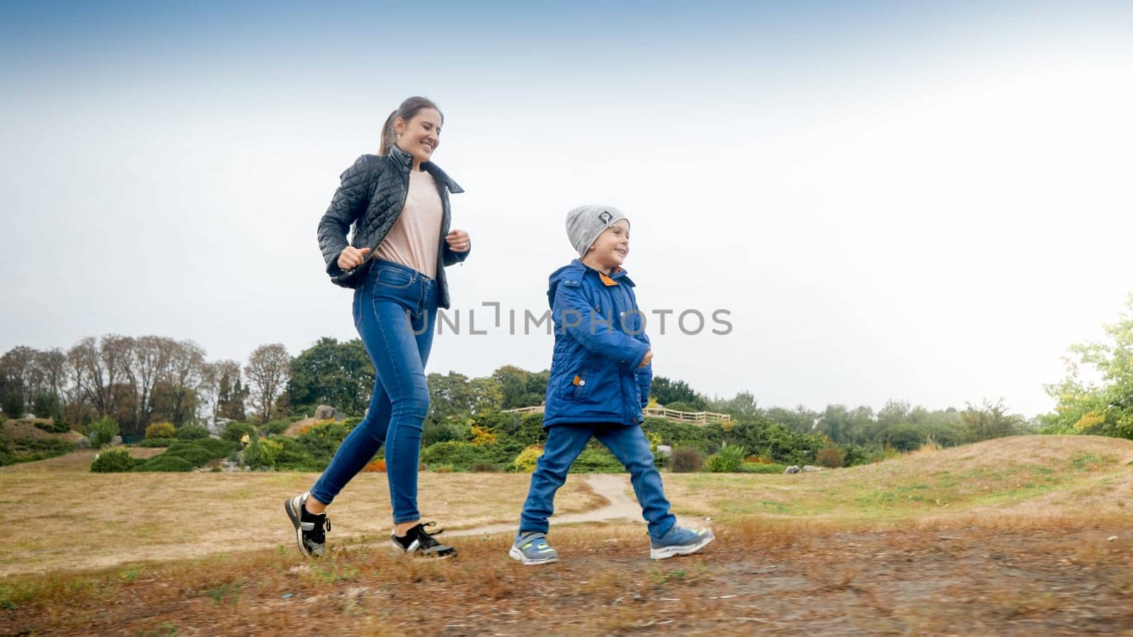 Happy smiling little boy with young mother walking on the field at autumn park.
