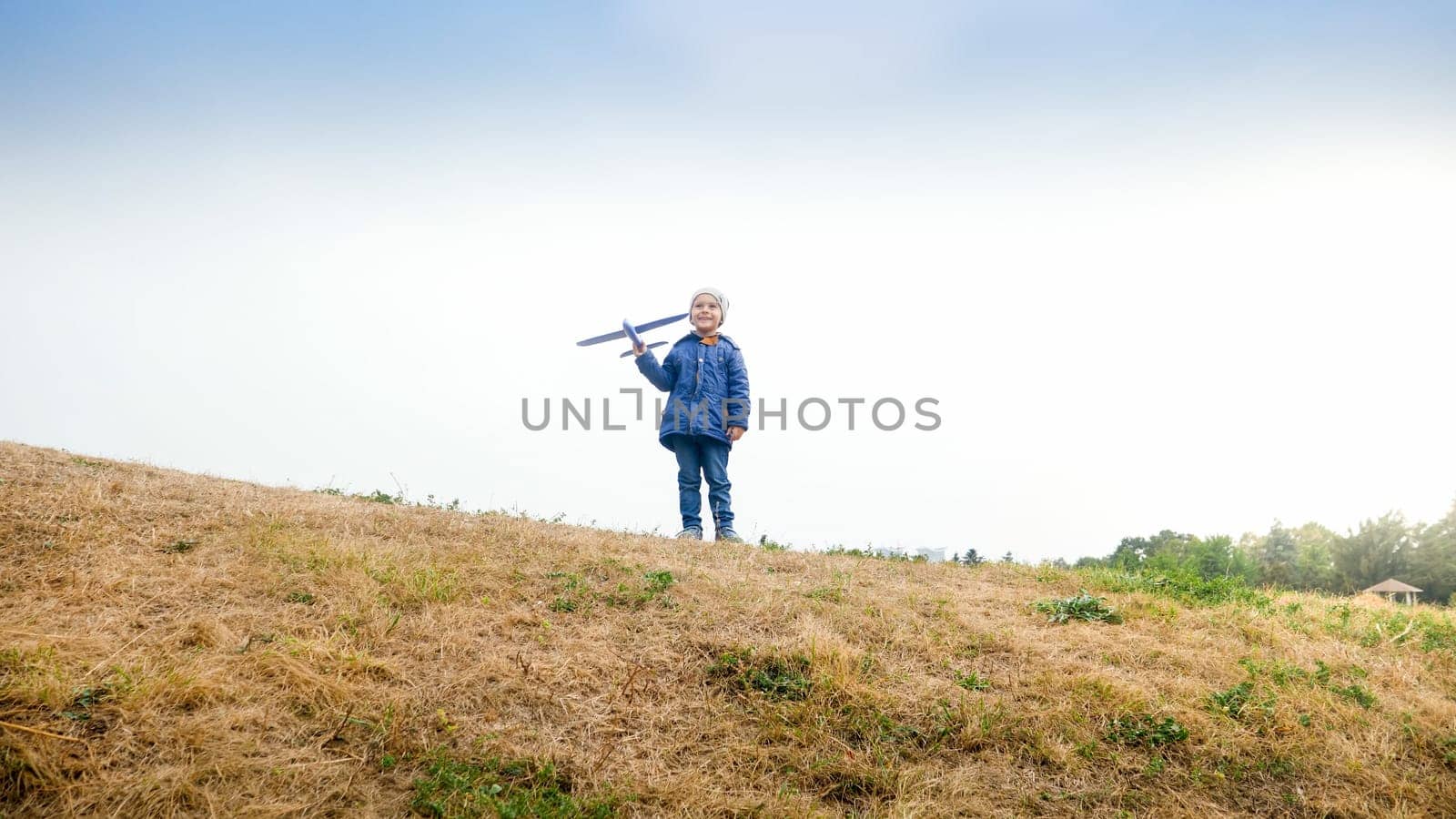 Happy smiling little boy standing on hill top with toy airplane.