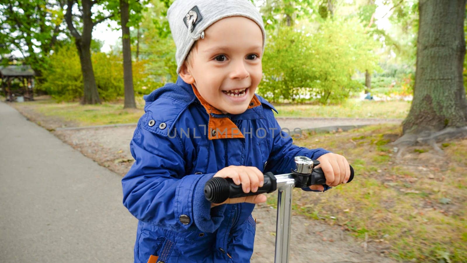 Portrait of smiling little boy smiling while riding on scooter at autumn park.