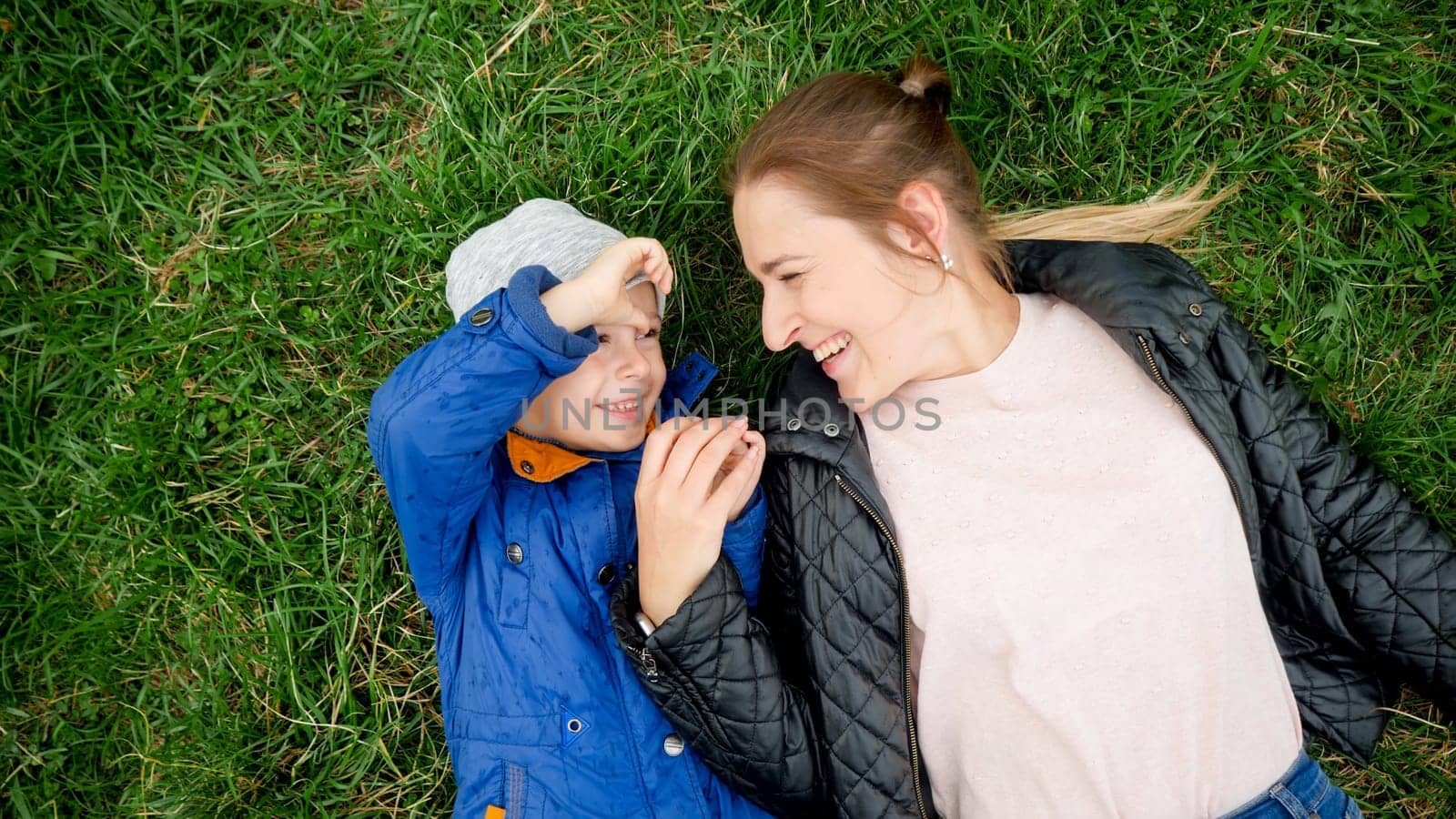 Portrait of happy smiling mother with little boy lying on grass and looking at each other.