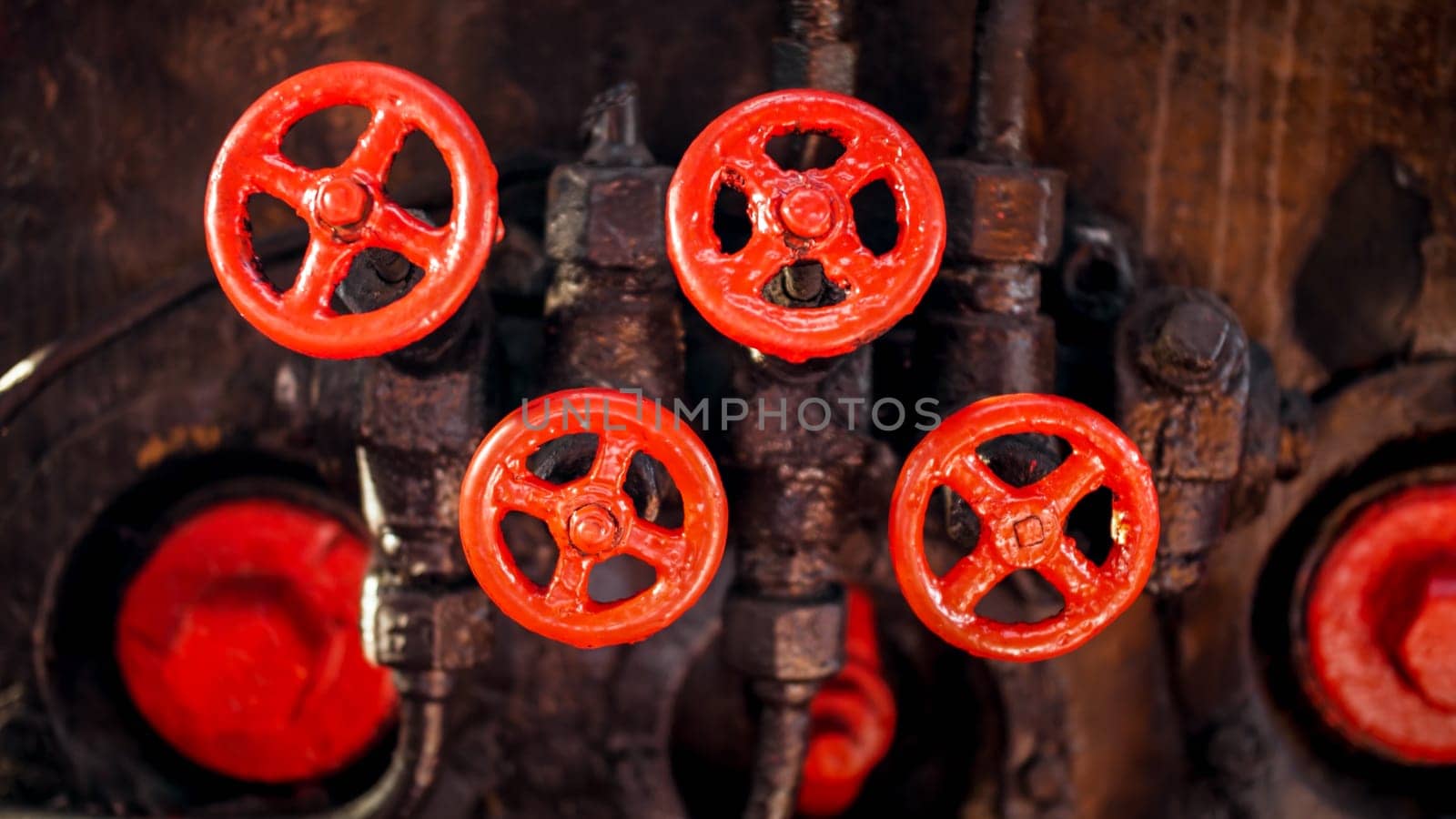 Closeup image of red painted vavles and black pipes of vintage high pressure system on factory
