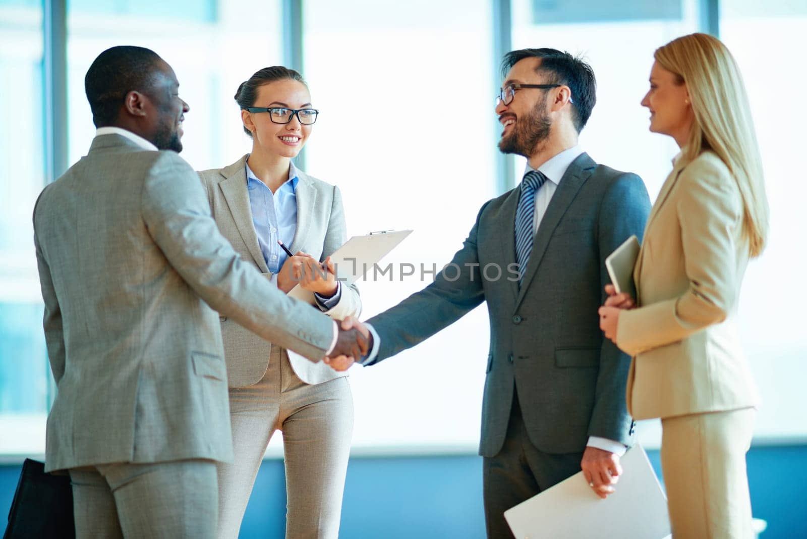 Happy businessmen handshaking with their two colleagues near by