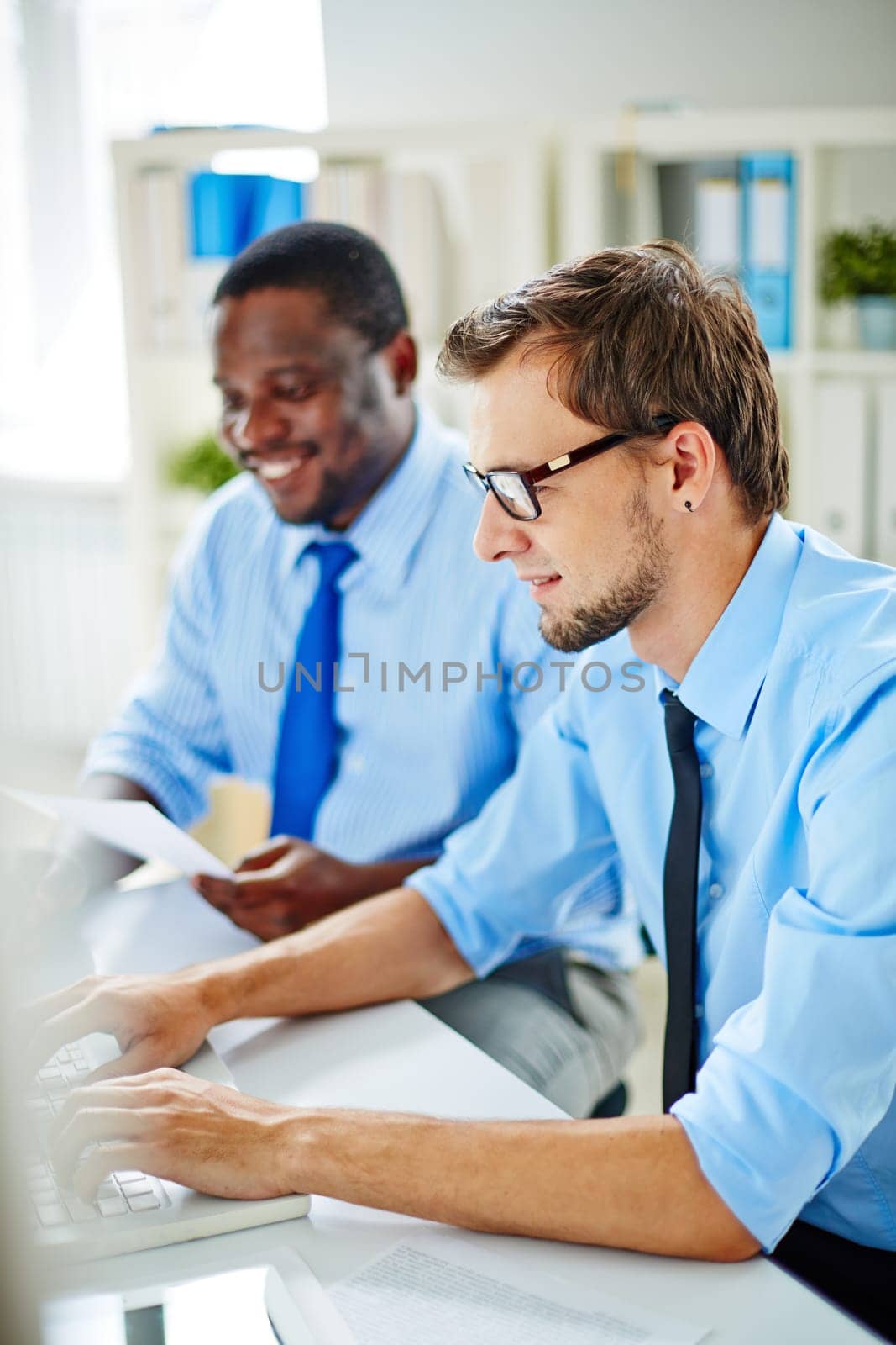 Young office worker typing on background of his colleague