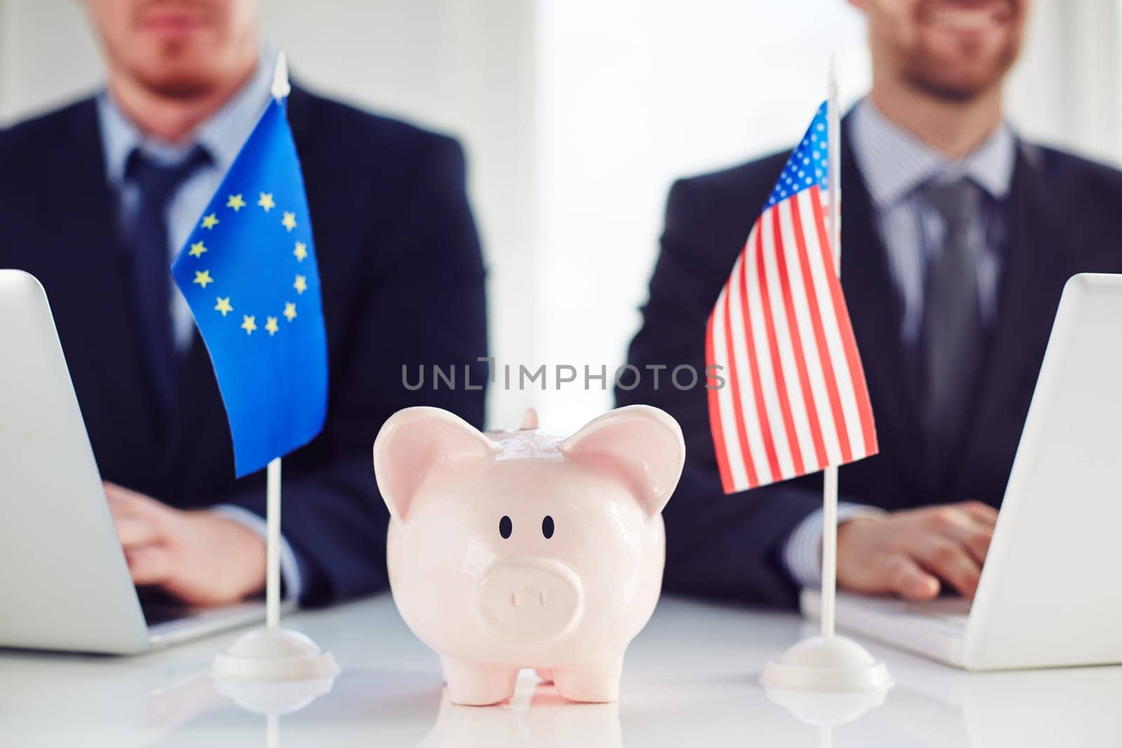Piggy bank between eu and American flag on background of businessmen typing