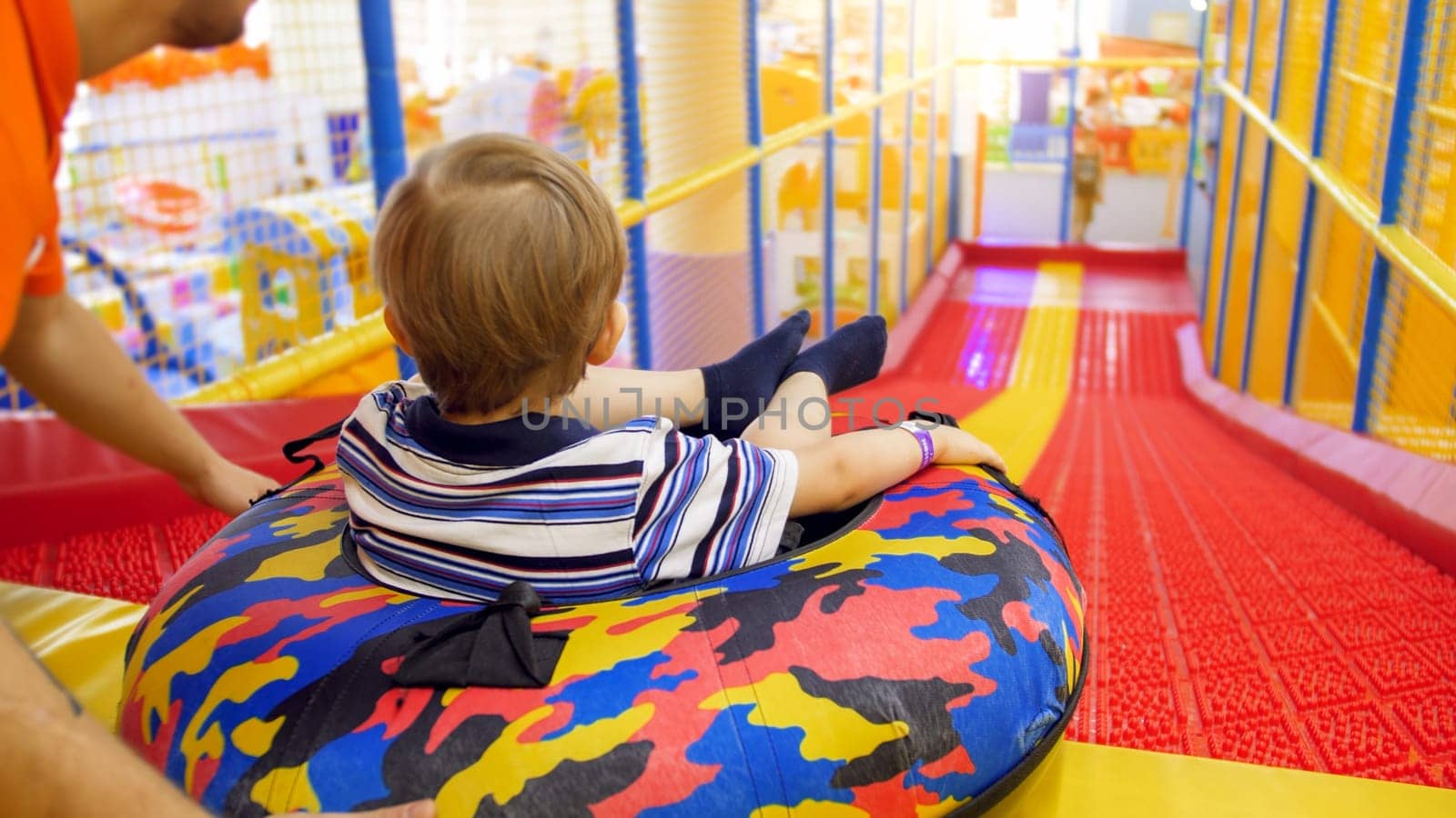 Cute little boy riding down the slide on inflatable donut ring in child's playing room at shopping mall.