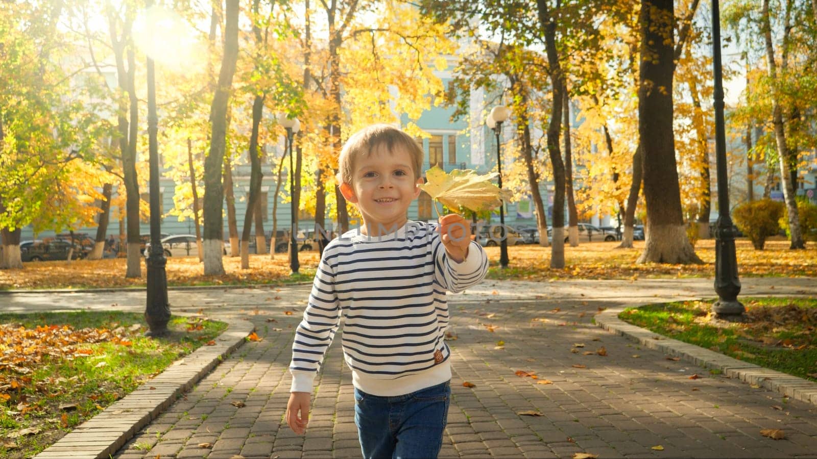 Portrait of cute little boy holding yellow autumn lef and running towards the camera at park.
