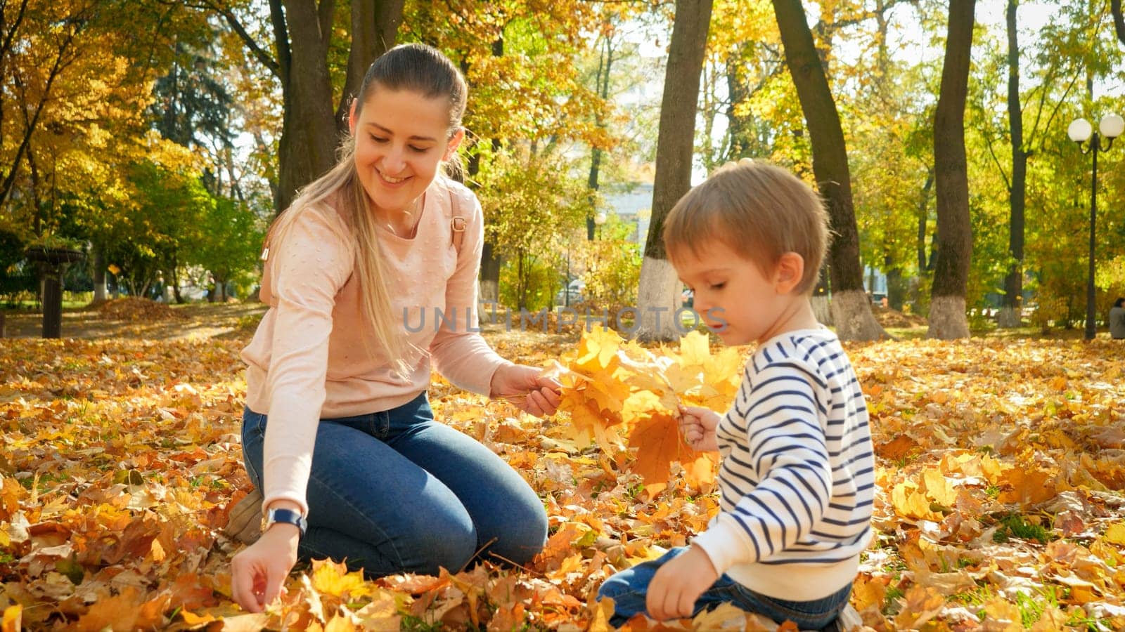 Happy family collecting and picking up golden tree leaves in beautiful autumn park.