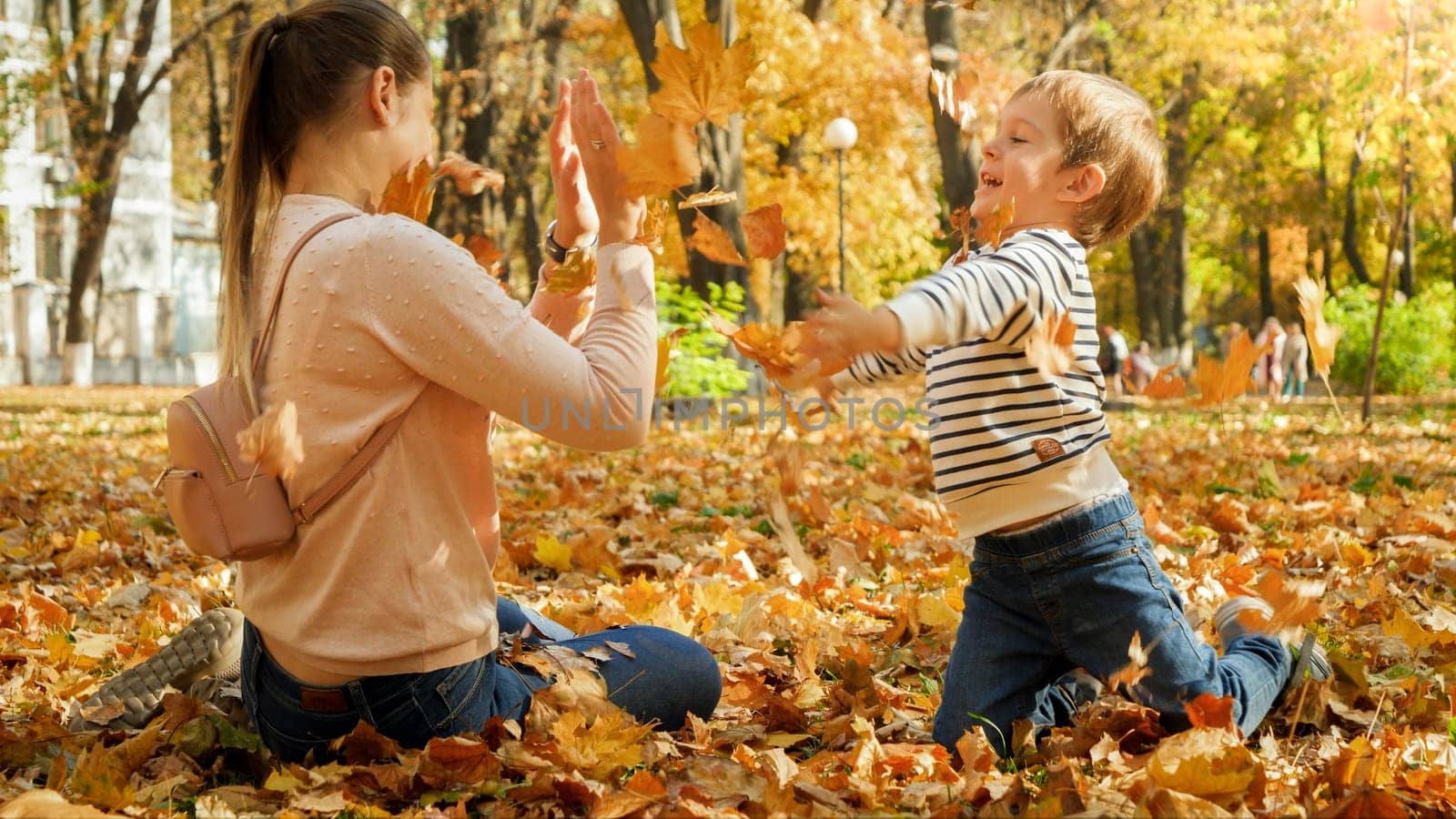 Little boy throwing fallen autumn leaves at his mother at park.