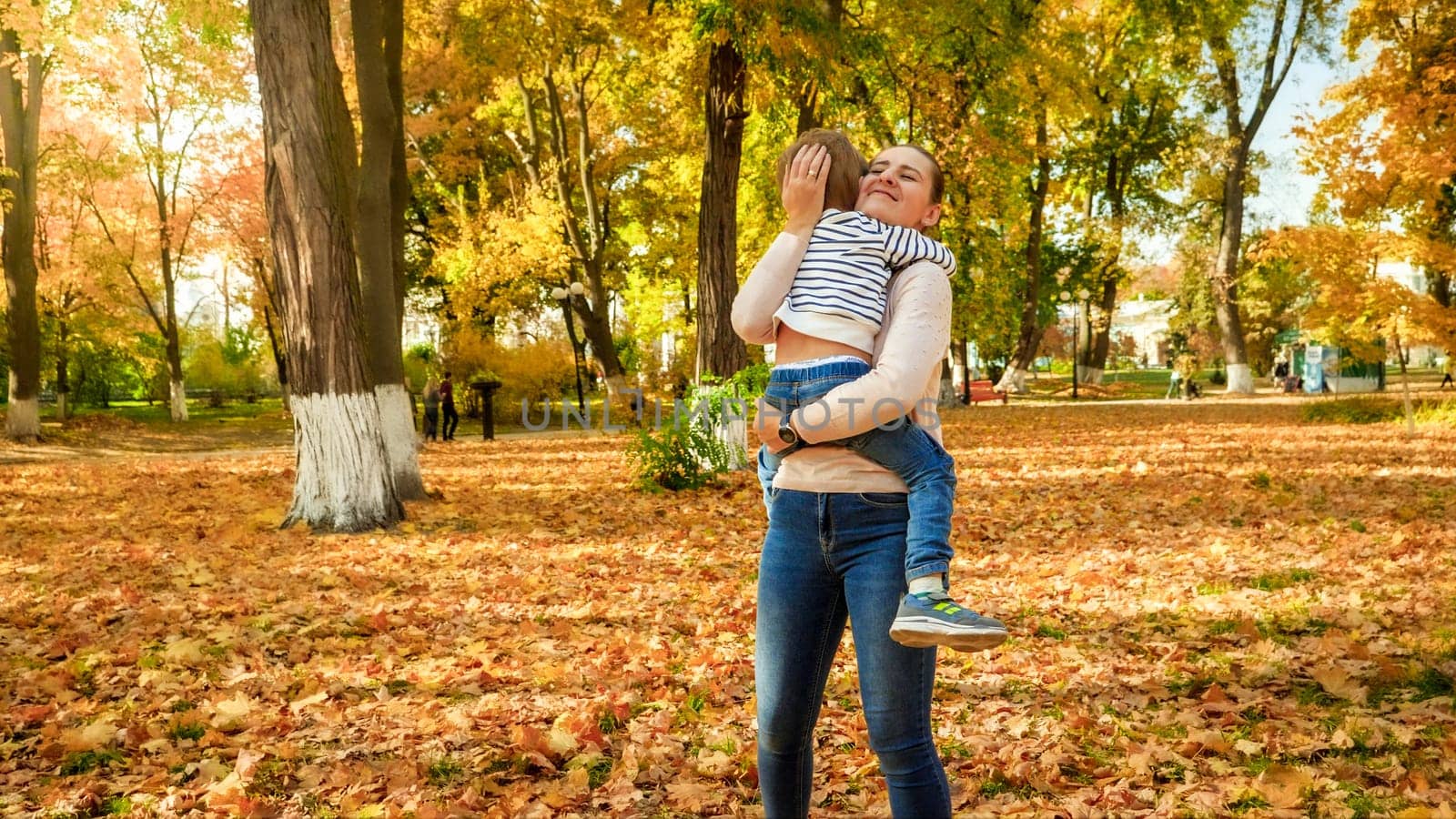 Beautiful smiling young mother hugging her little son in autumn park.