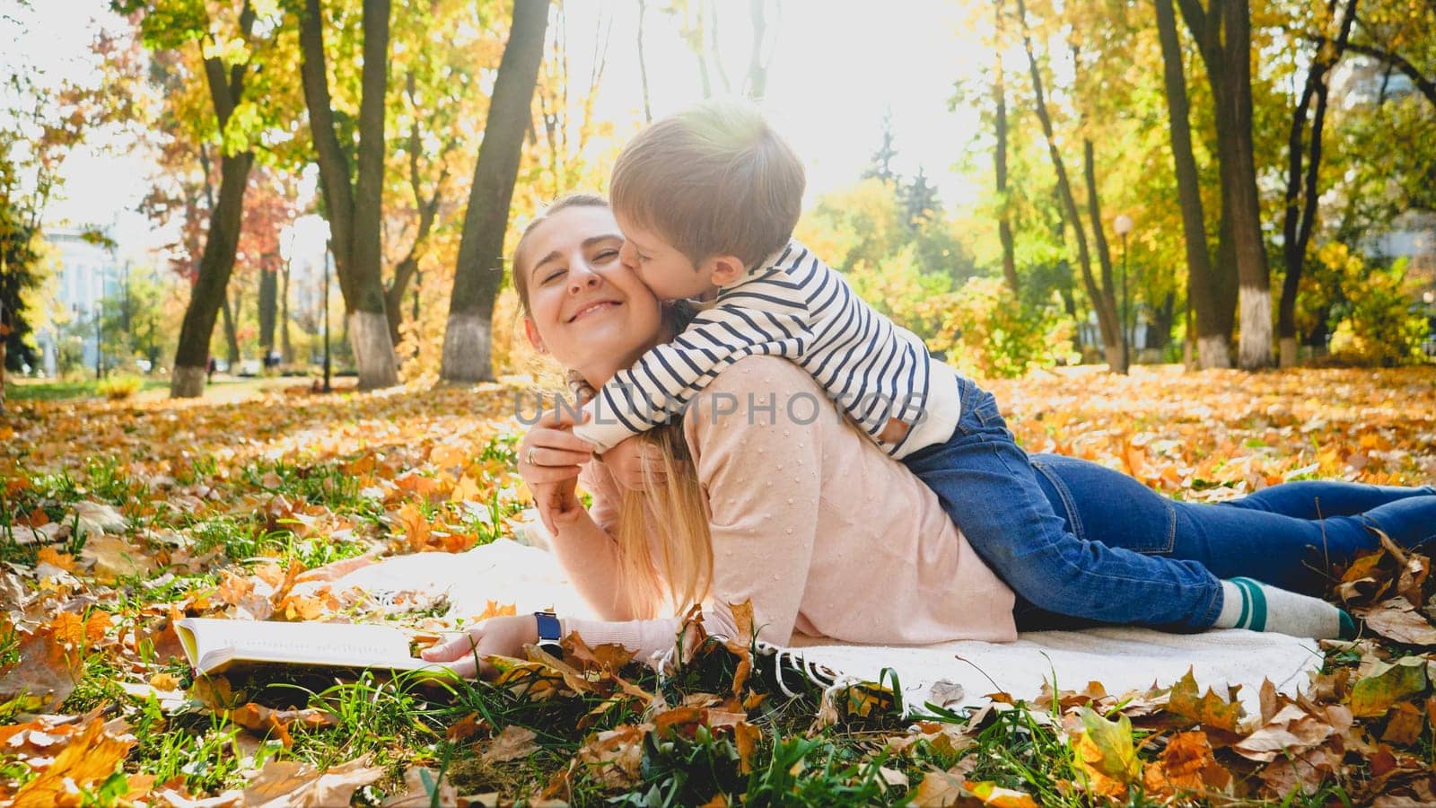 Portrait of little son kissing his mother in cheek at autumn park.