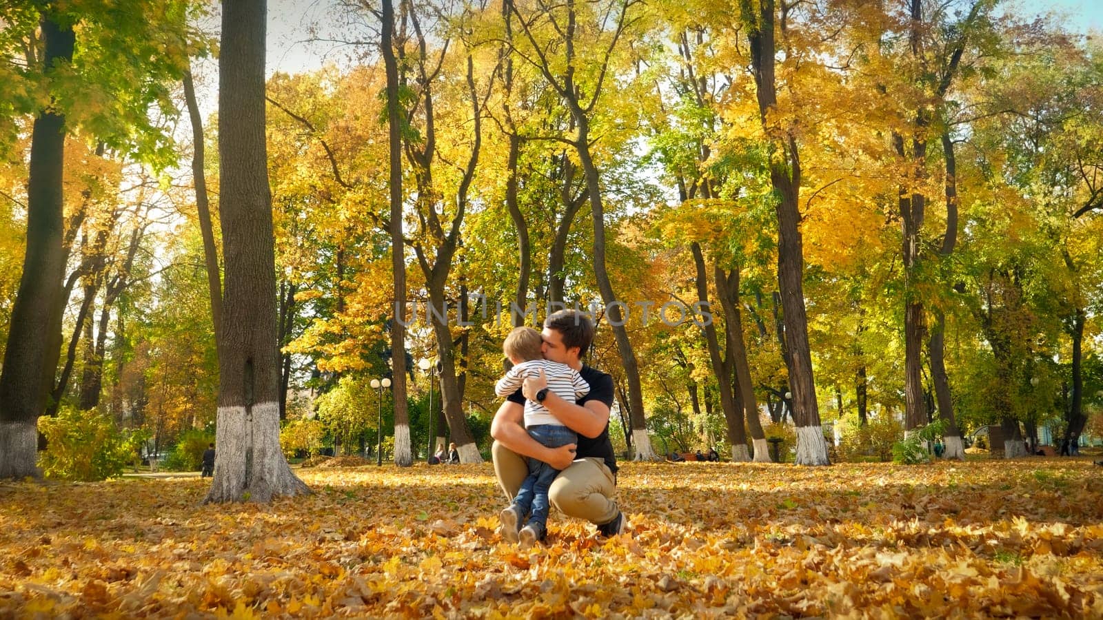 Adorable little boy hugging and kissing his father in autumn park.