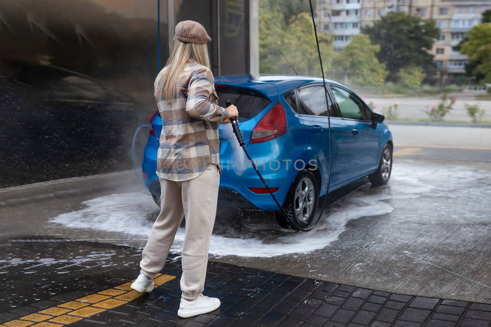 Woman washing a car in a self-service car wash station with wahing foam. Wash car self-service station.