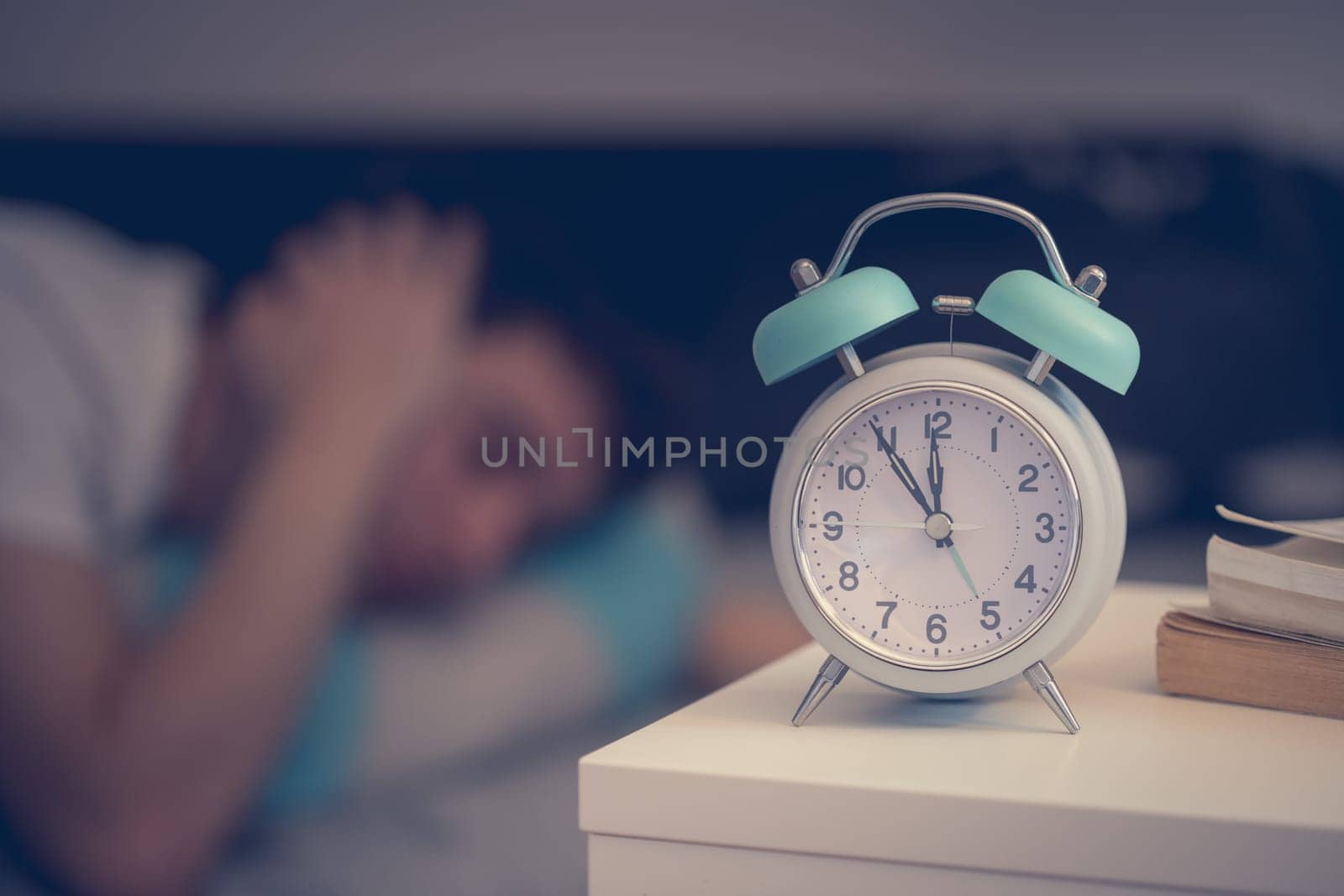 White alarm clock on the bedside table. Young man sleeps in the background.