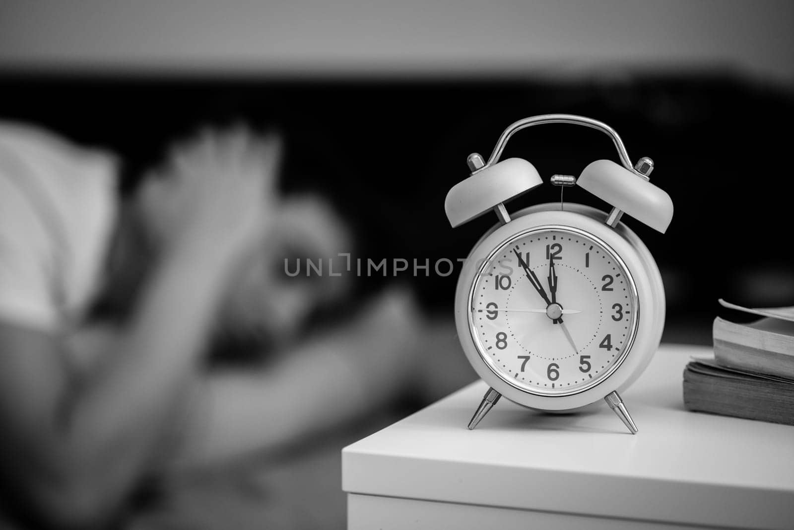 White alarm clock on the bedside table. Young man sleeps in the background.