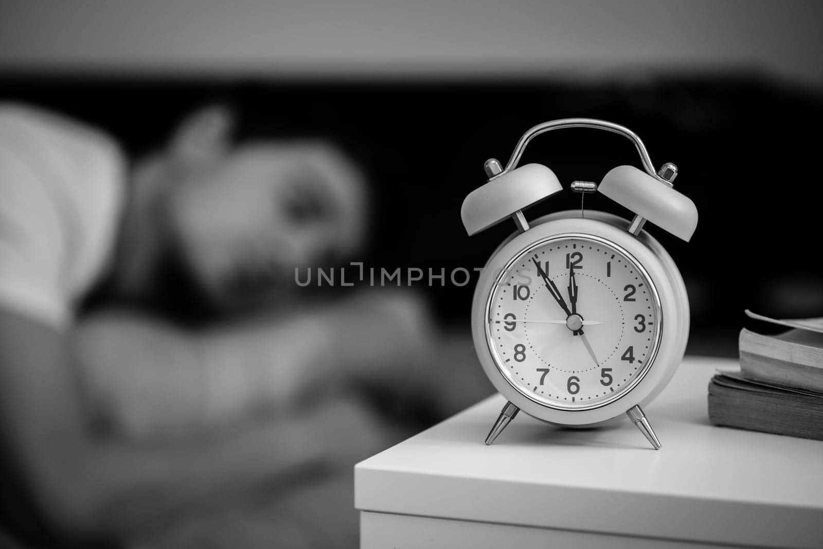White alarm clock on the bedside table. Young man sleeps in the background.