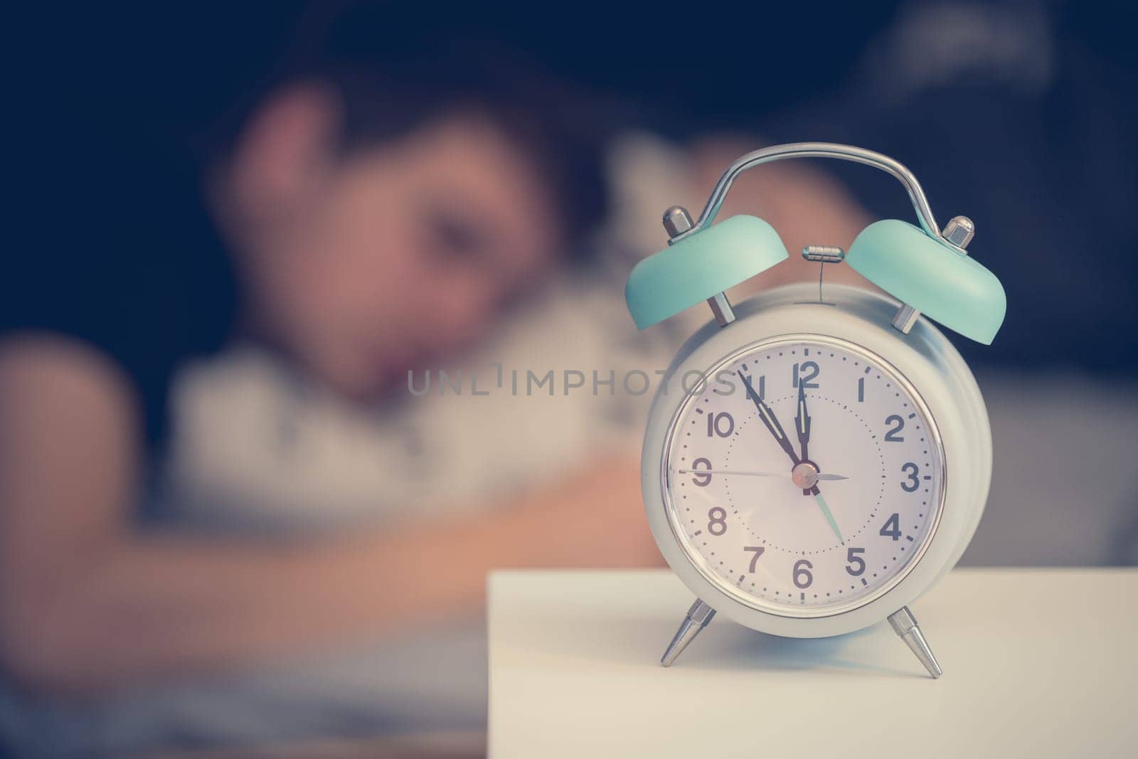 White alarm clock on the bedside table. Young man sleeps in the background.