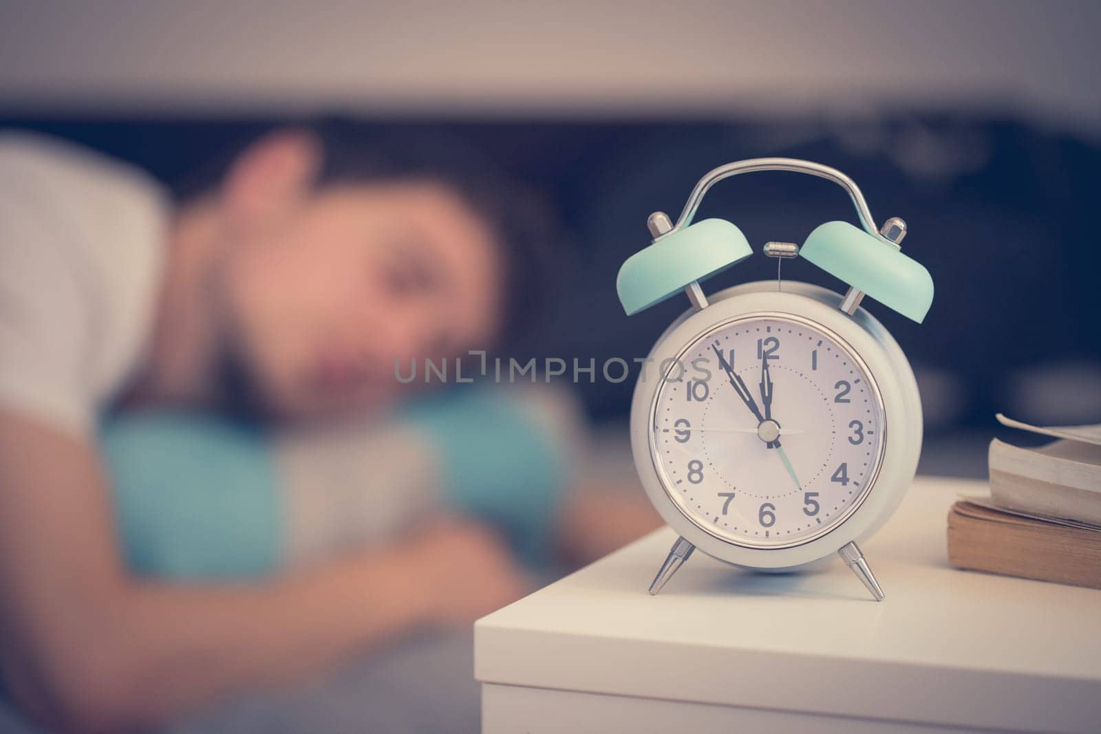 White alarm clock on the bedside table. Young man sleeps in the background.