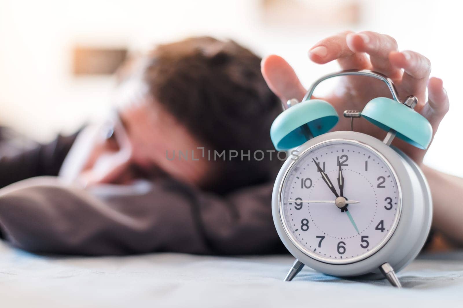 White alarm clock in the morning. Young man wakes up.
