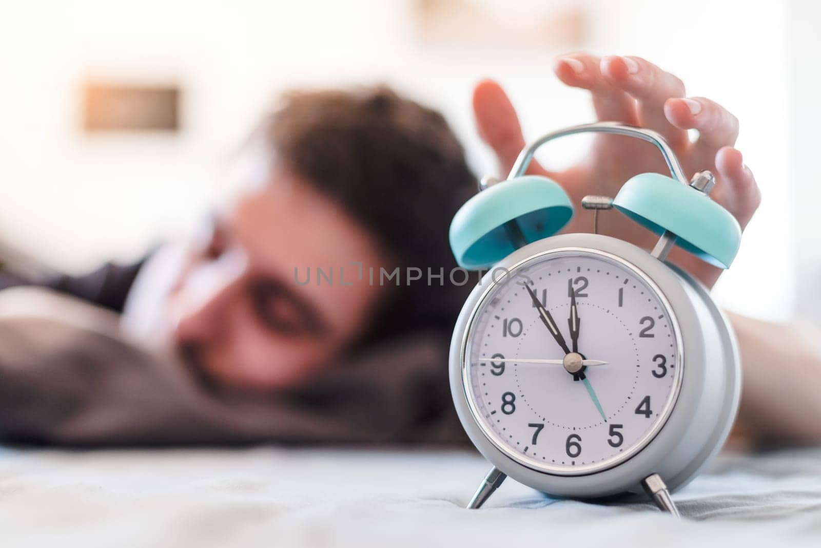 White alarm clock in the morning. Young man wakes up.