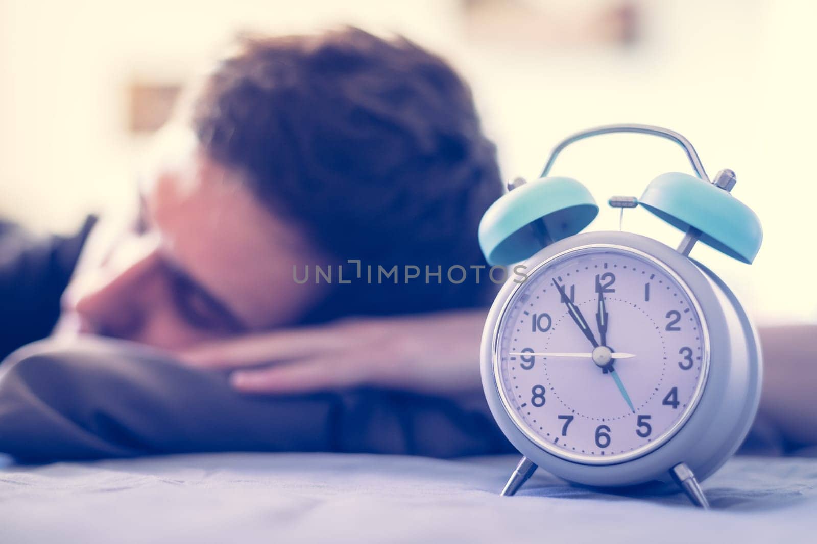 White alarm clock in the morning. Young man sleeps in the background.