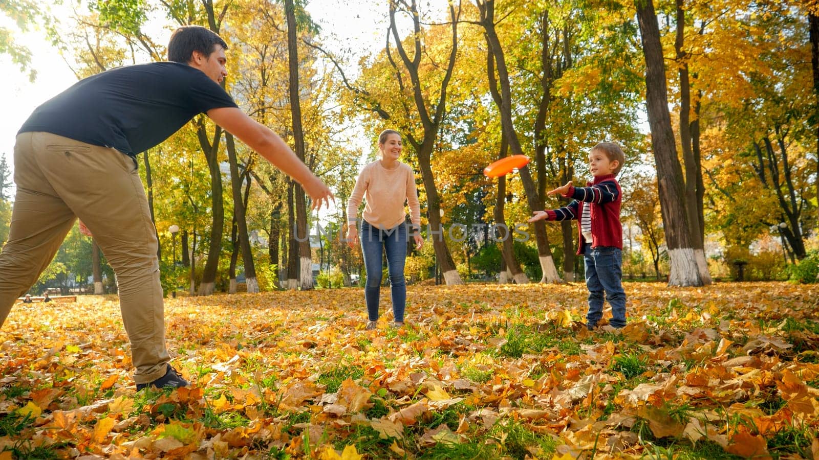 Happy smiling family playing with frisbee in autumn park.