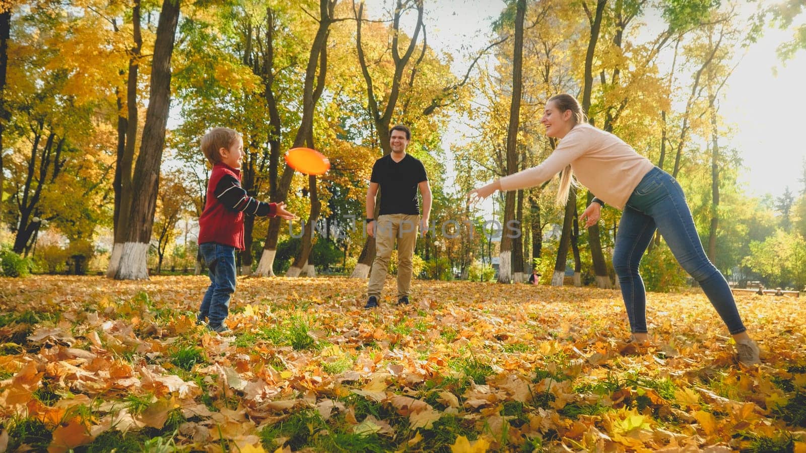 Beautiful young mother throwing frisbee to her little son at autumn park.