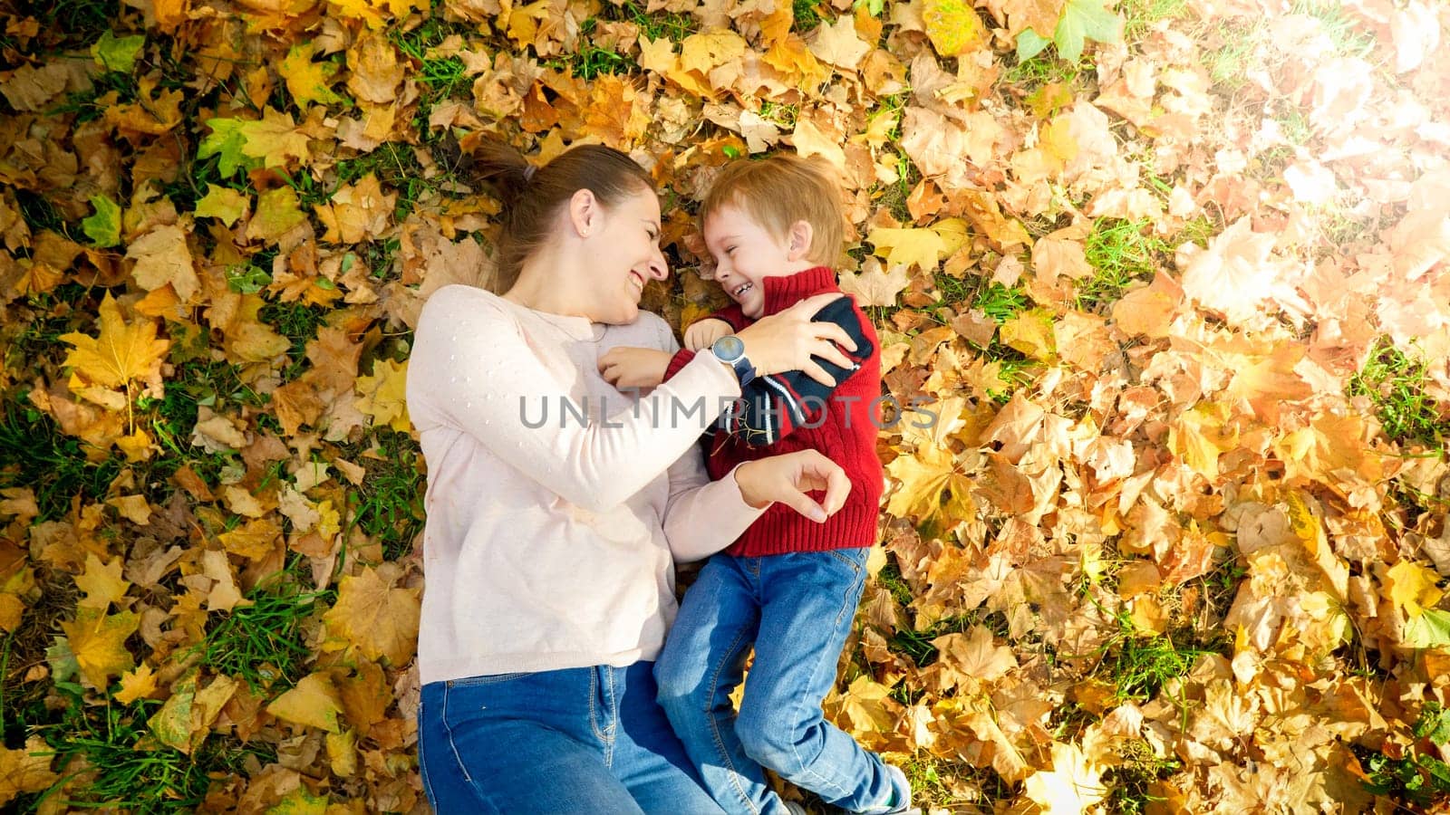 Happy smiling and laughing family lying on ground covered with yellow fallen autumn leaves at park.