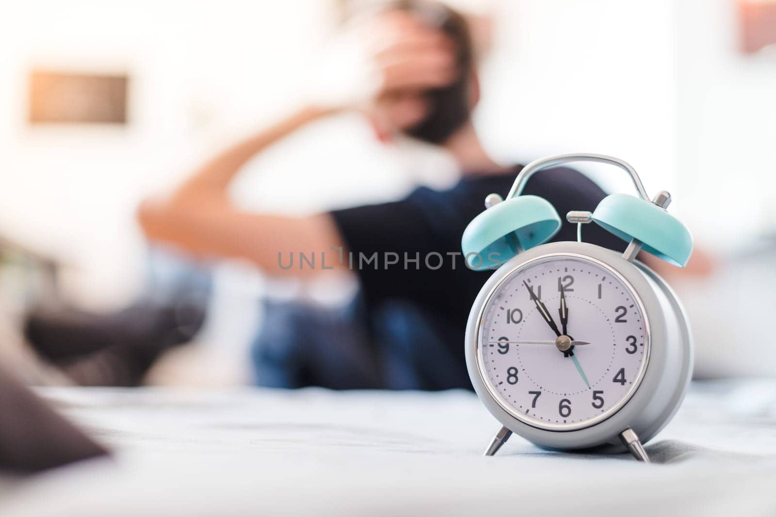 White alarm clock in the morning. Young man wakes up and stretches in the background.