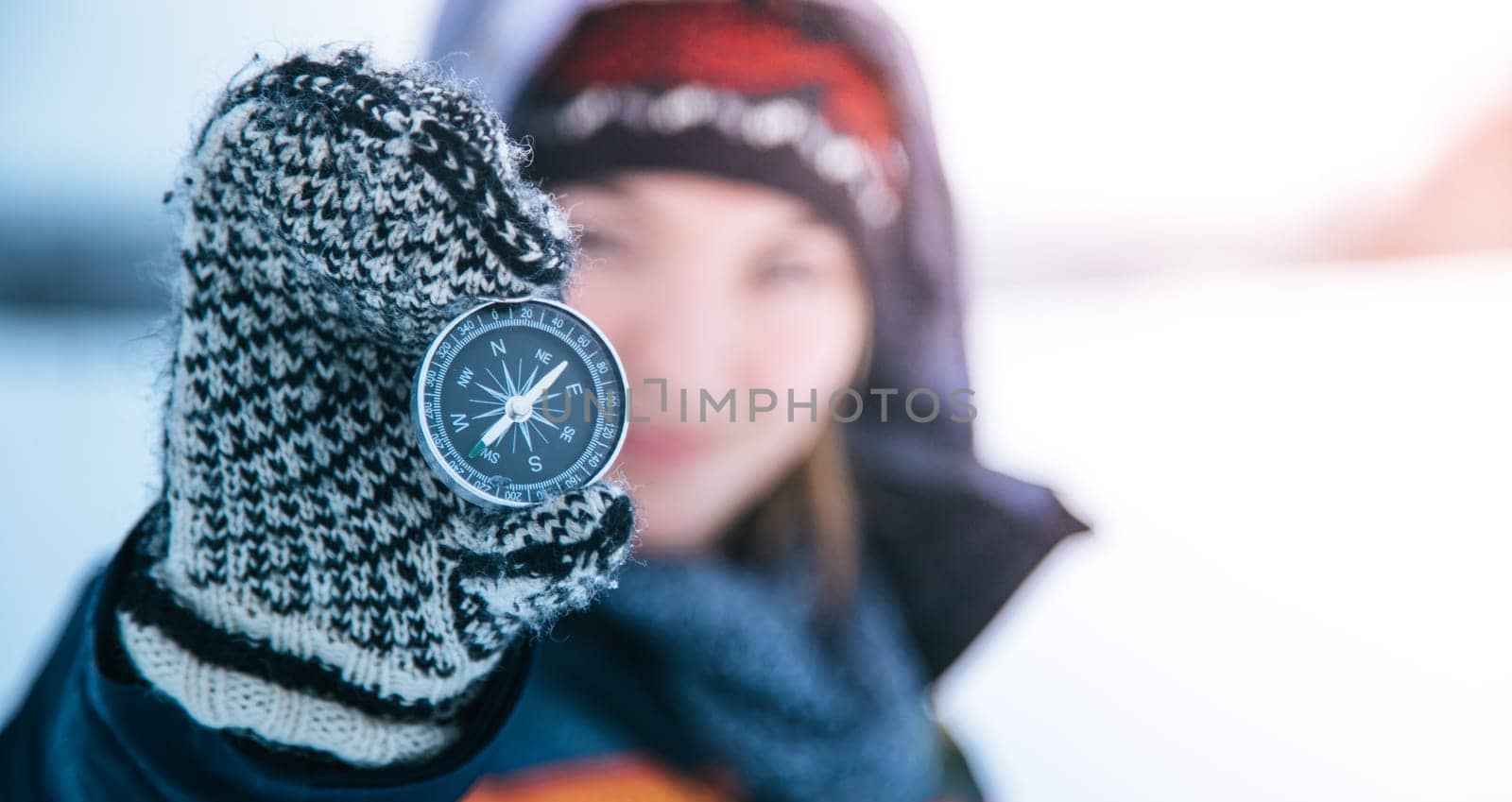 Young smiling woman holds up a compass. Wintertime, gloves and hood.