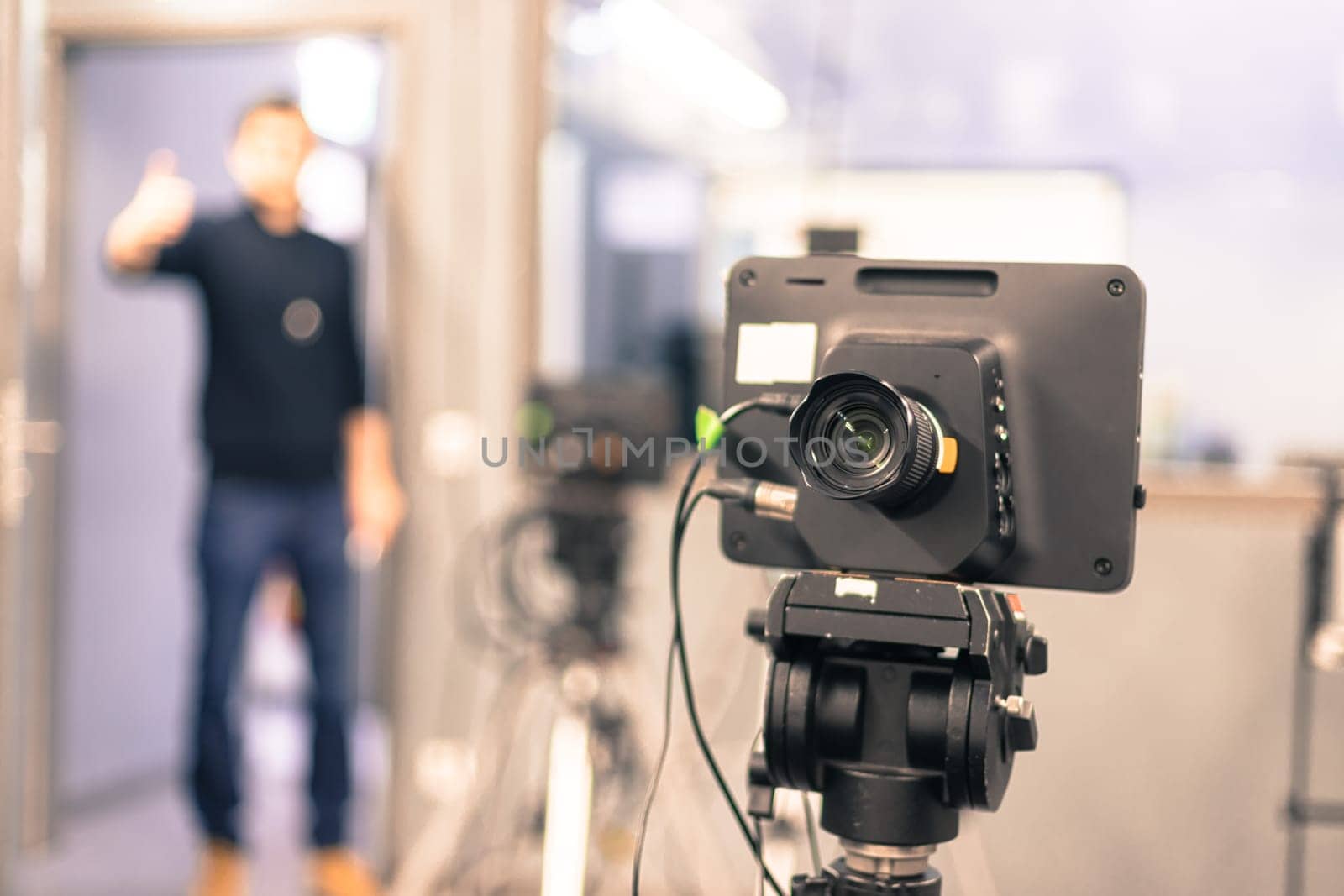 Lens of a film camera in an television broadcasting studio, spotlights and equipment, director in the background