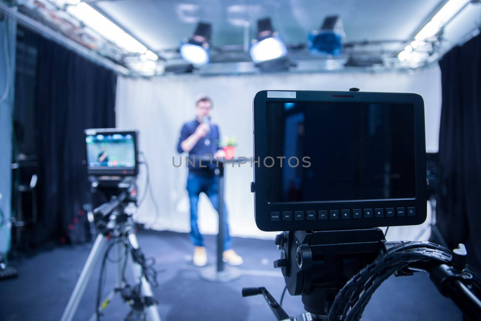 Male journalist in a television studio talks into a microphone, film cameras