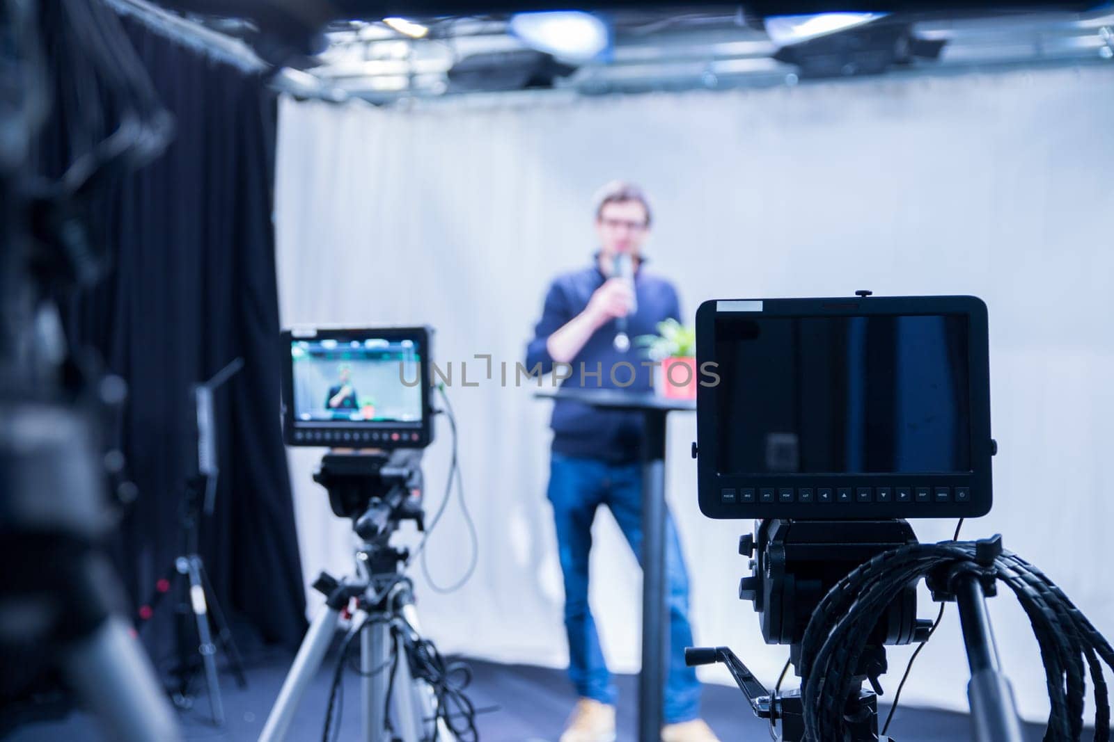 Male journalist in a television studio talks into a microphone, film cameras