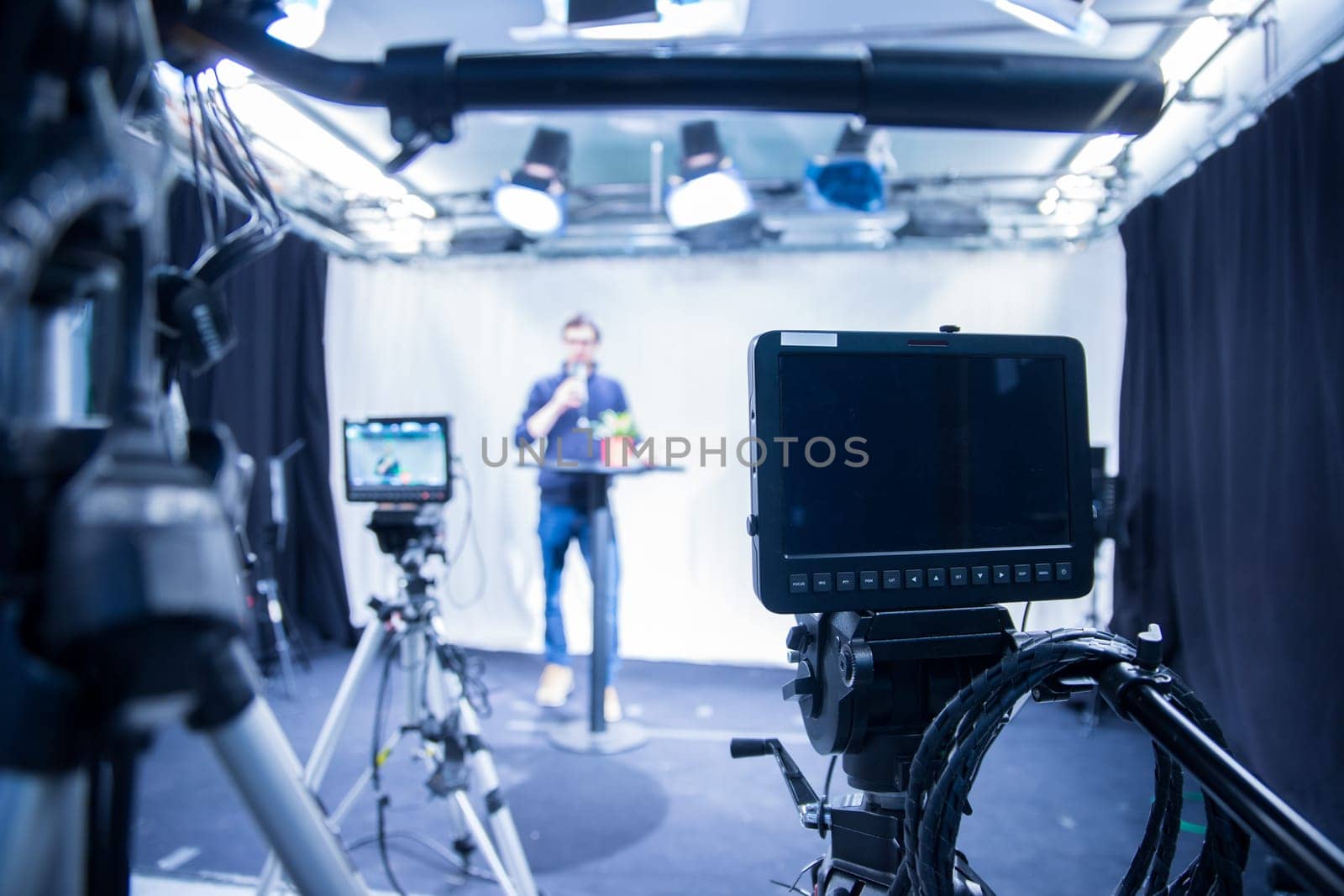 Male journalist in a television studio talks into a microphone, film cameras