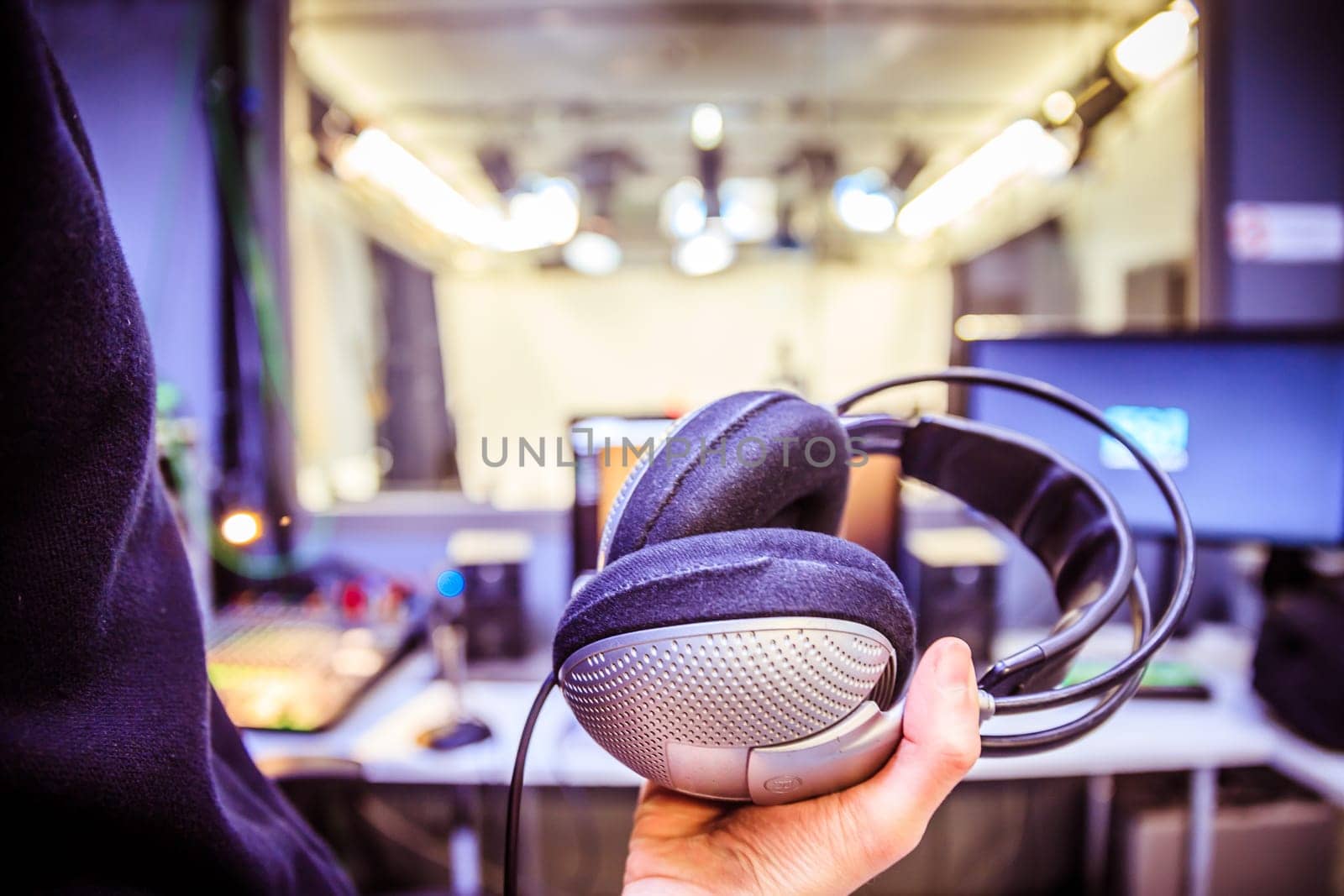 Young man holds headphones in the recording studio. Buttons, studio, screens and equipment in the blurry background