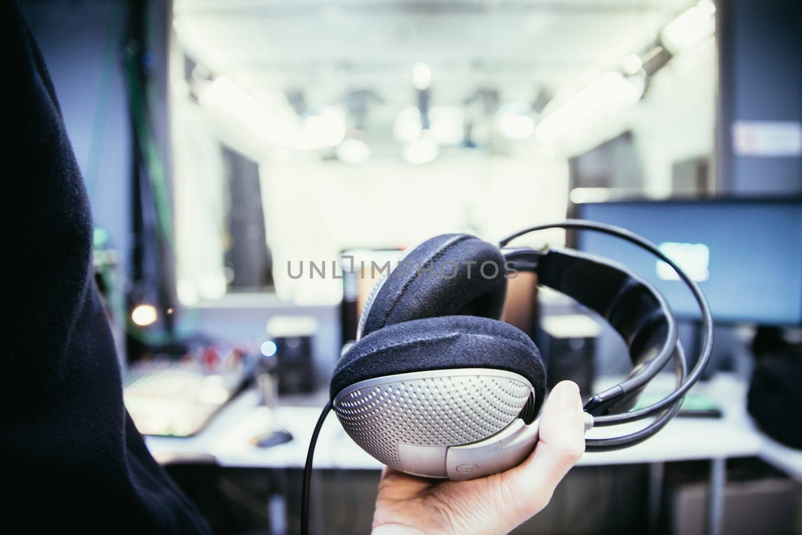 Young man holds headphones in the recording studio. Buttons, studio, screens and equipment in the blurry background