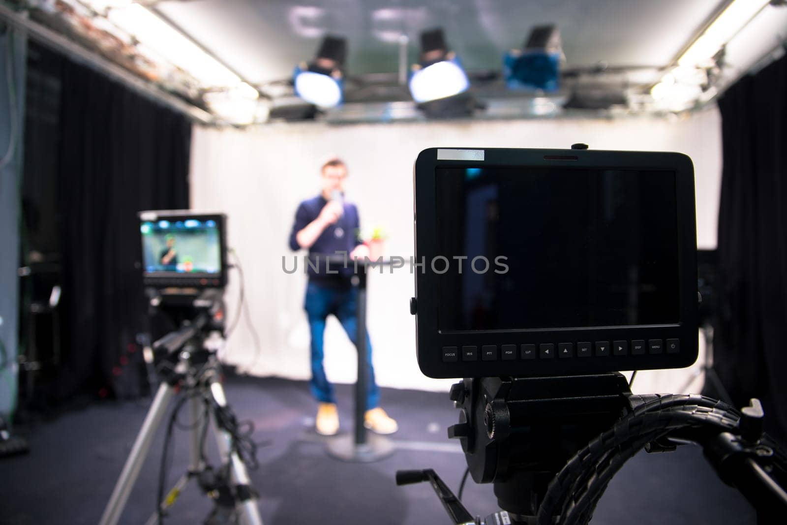 Male journalist in a television studio talks into a microphone, film cameras