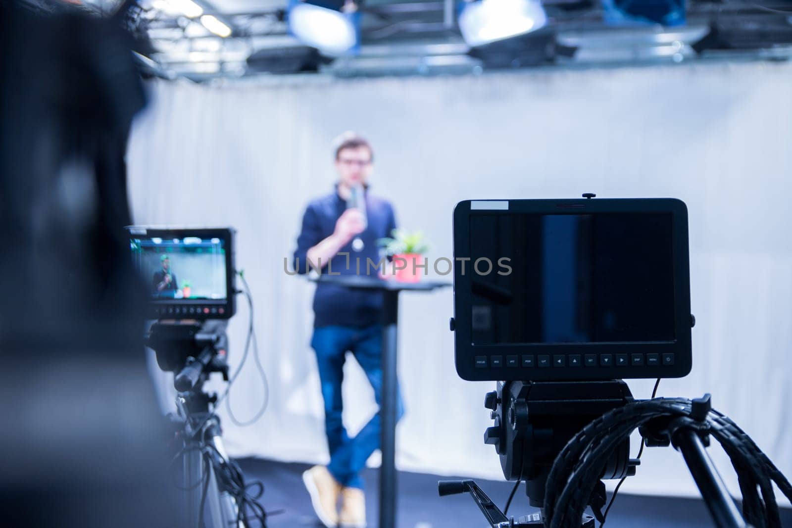 Male journalist in a television studio talks into a microphone, film cameras