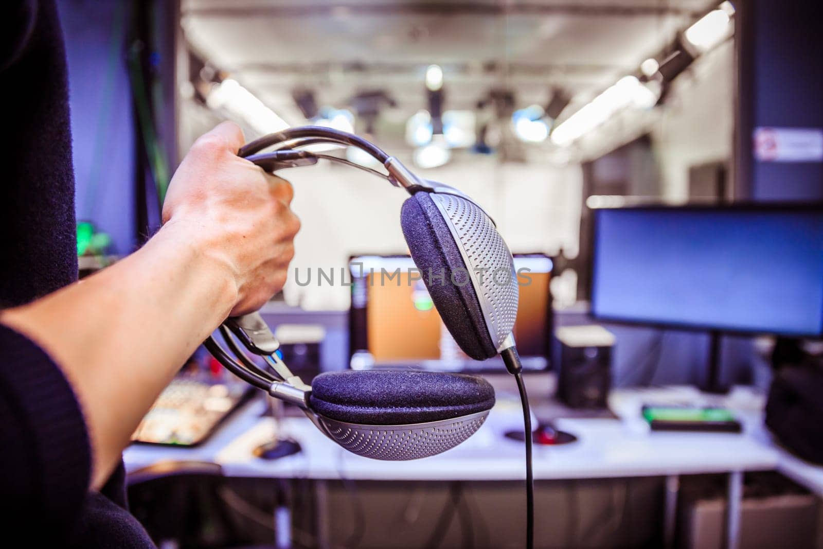 Young man holds headphones in the recording studio. Buttons, studio, screens and equipment in the blurry background