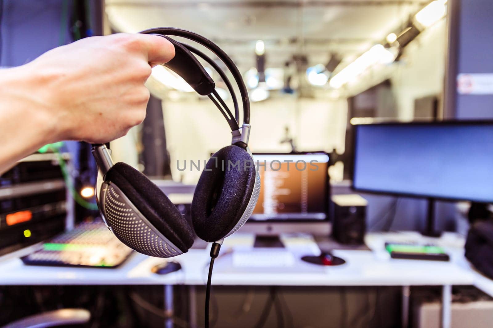 Young man holds headphones in the recording studio. Buttons, studio, screens and equipment in the blurry background