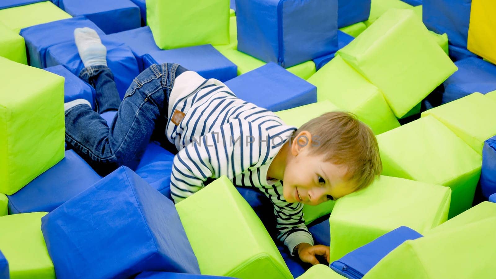 Portrait of smiling toddler boy crawling and having fun with soft cubes in amusement park.